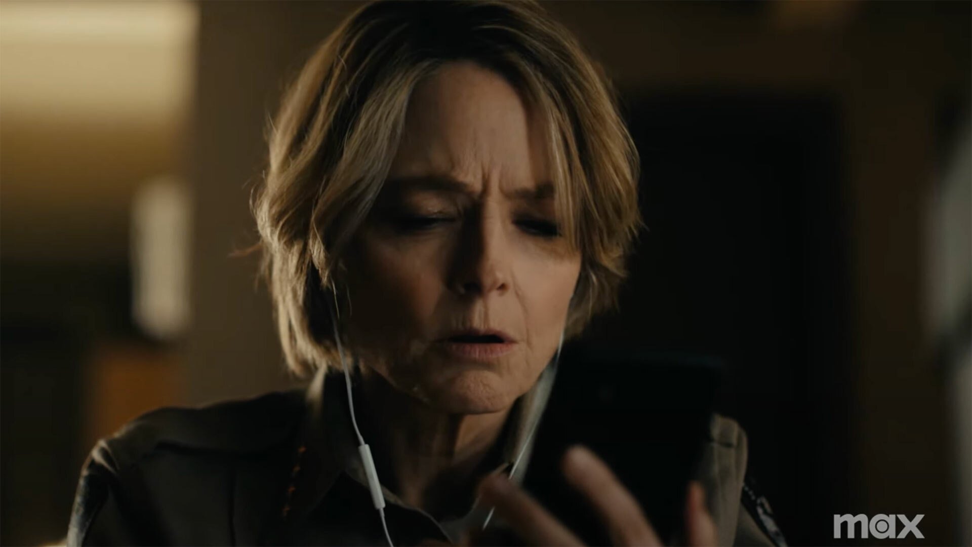 A woman wearing headphones frowns while looking at a phone.