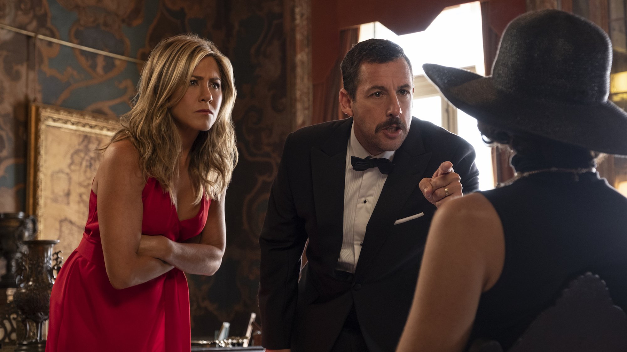 Jennifer Aniston and Adam Sandler point accusatory fingers at a seated Gemma Arterton in the film "Murder Mystery"