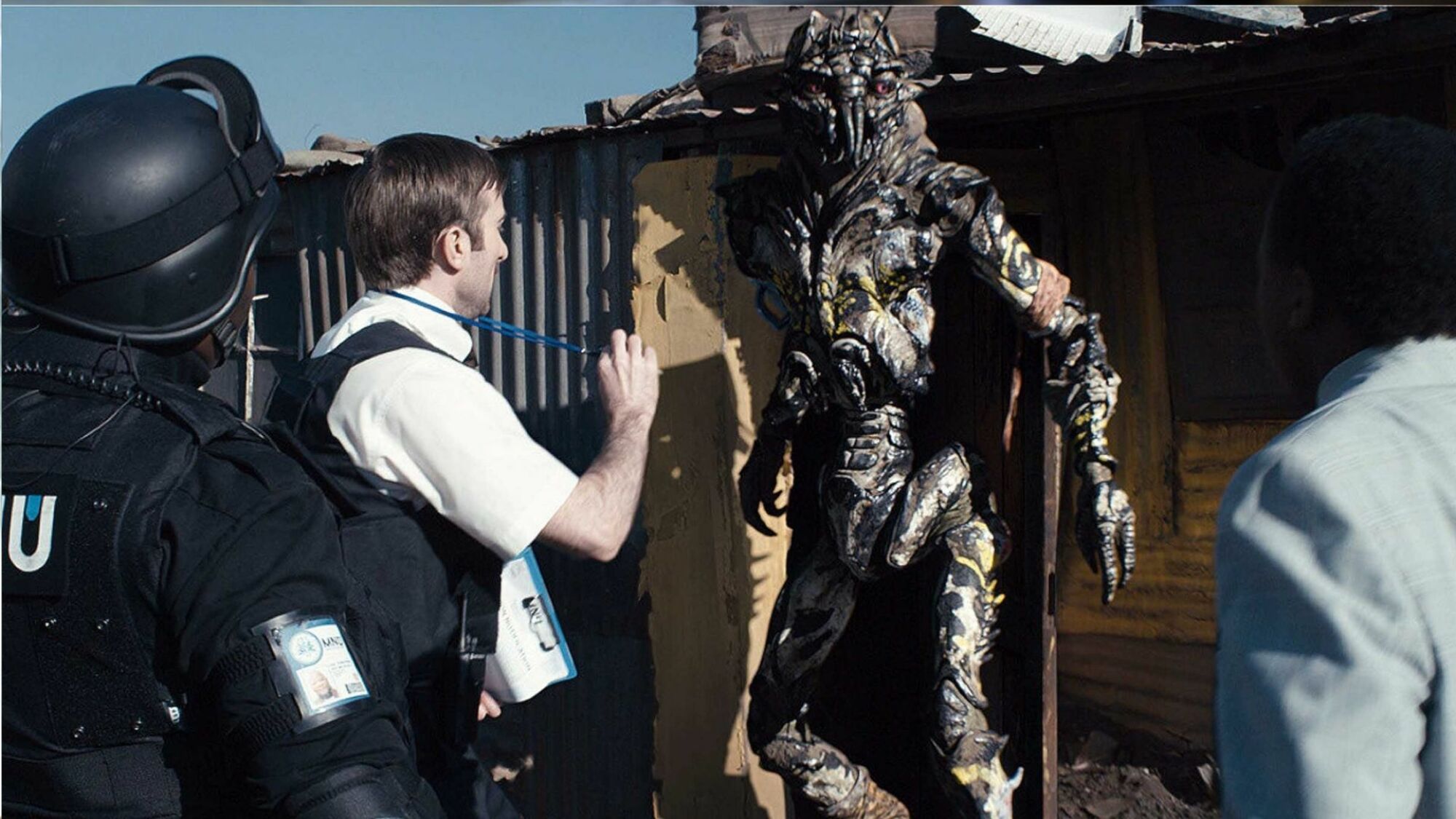 A government agent presents his badge to an extraterrestrial outside a hovel.