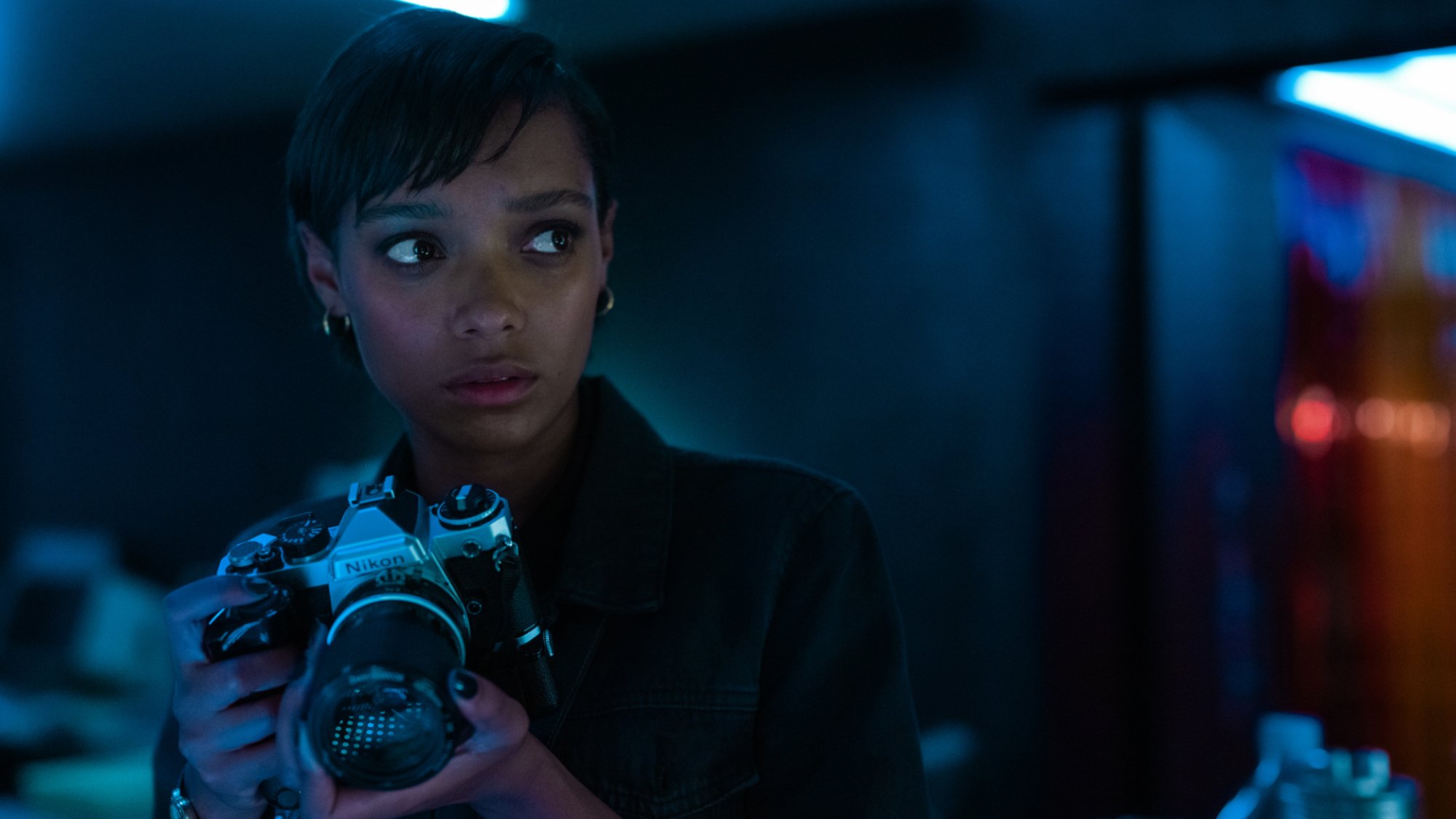 A woman with a camera looks worried in a dark room.