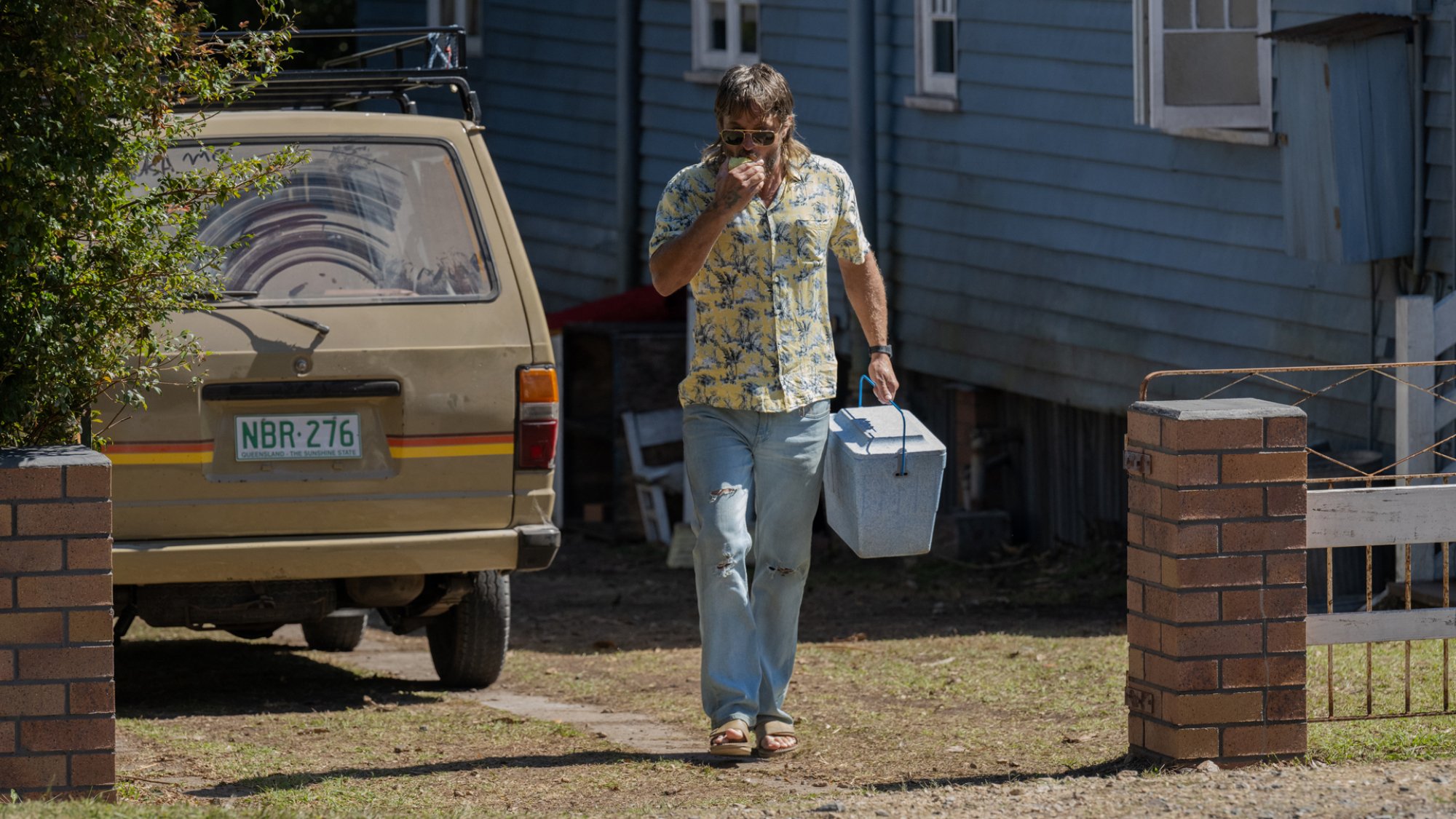 A man holding a cooler walks out of his driveway.