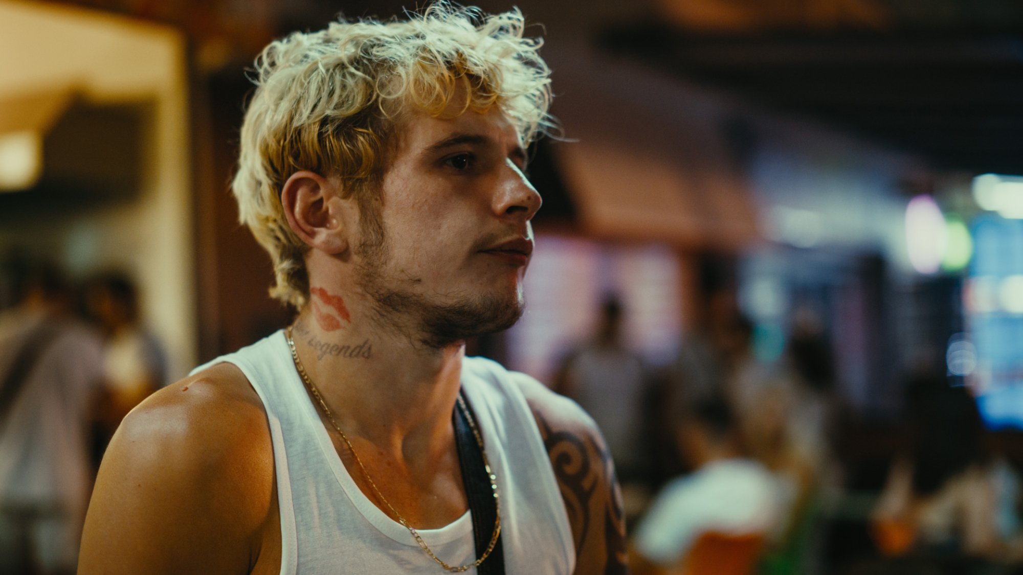 A teen boy with bleached hair and a neck tattoo of a lipstick mark looks concerned.