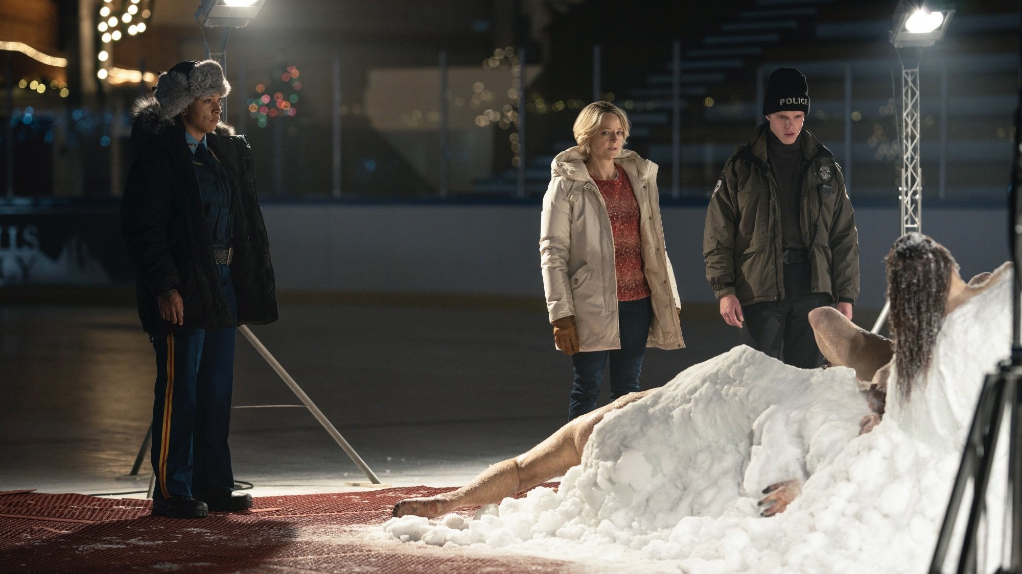 Two women and one man in police uniforms inspect a frozen clump of bodies thawing on an ice rink.
