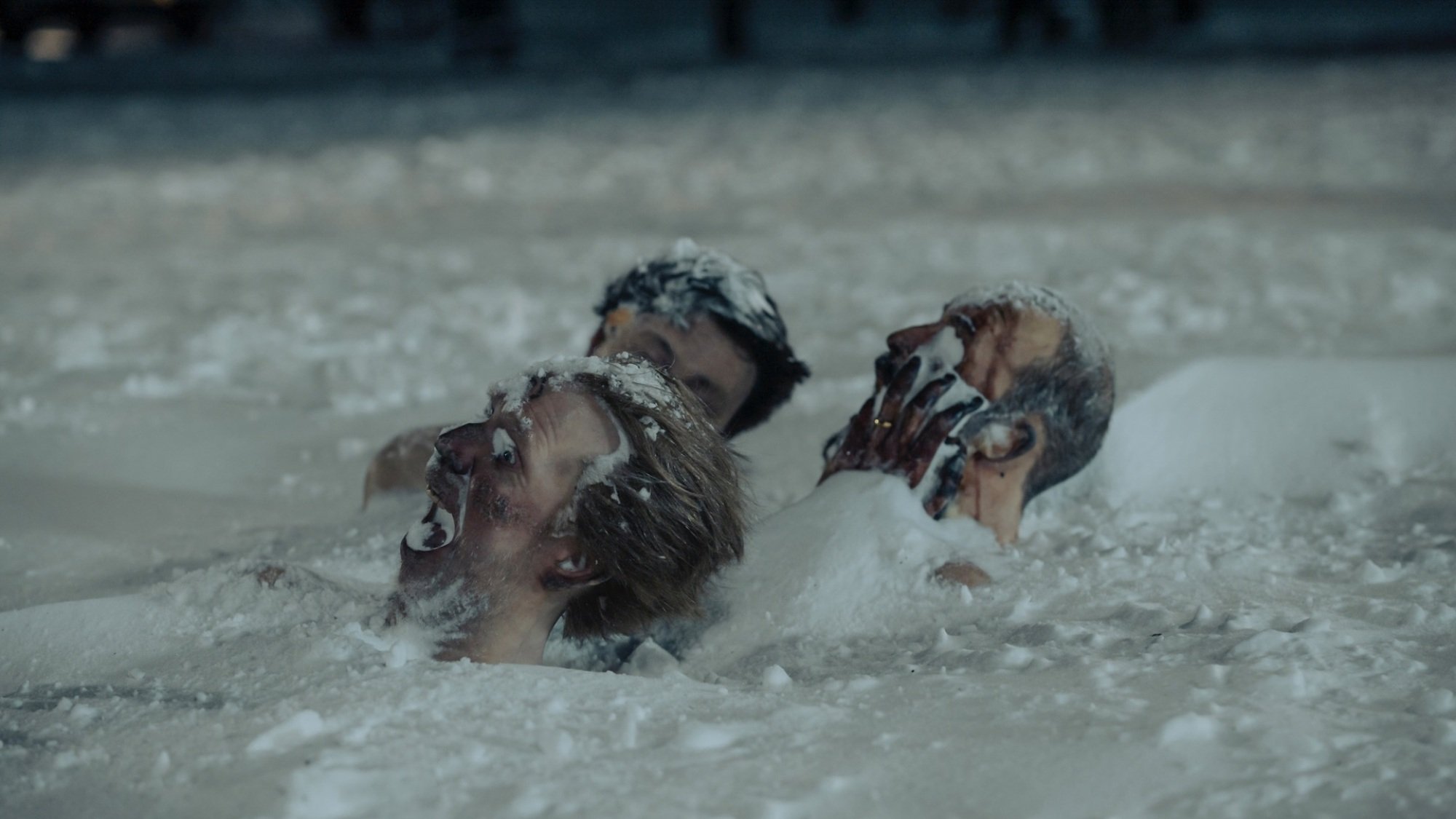 Three men's heads stick out of the snowy ground, frost-bitten and frozen in expressions of fear.