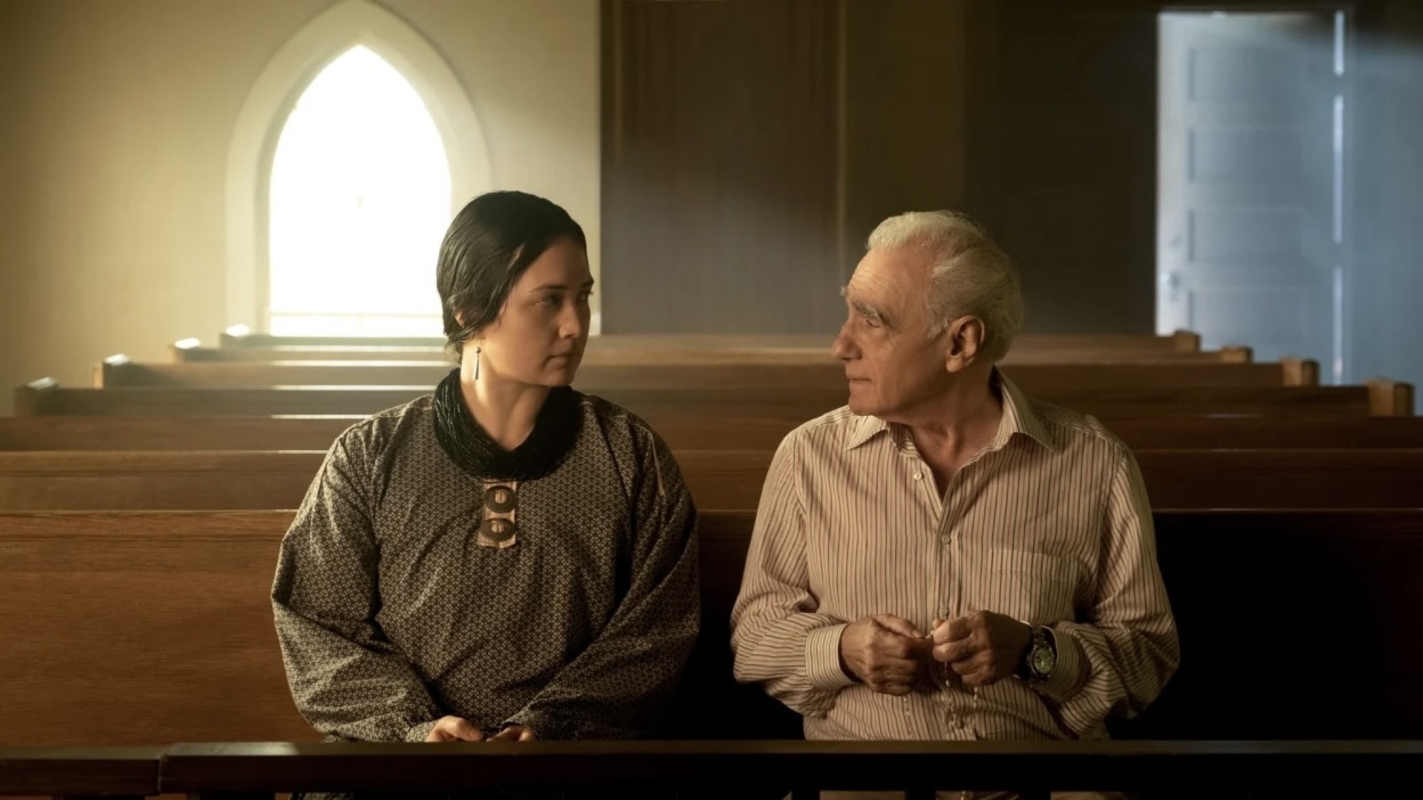 A man and woman sit in church pews talking to each other.