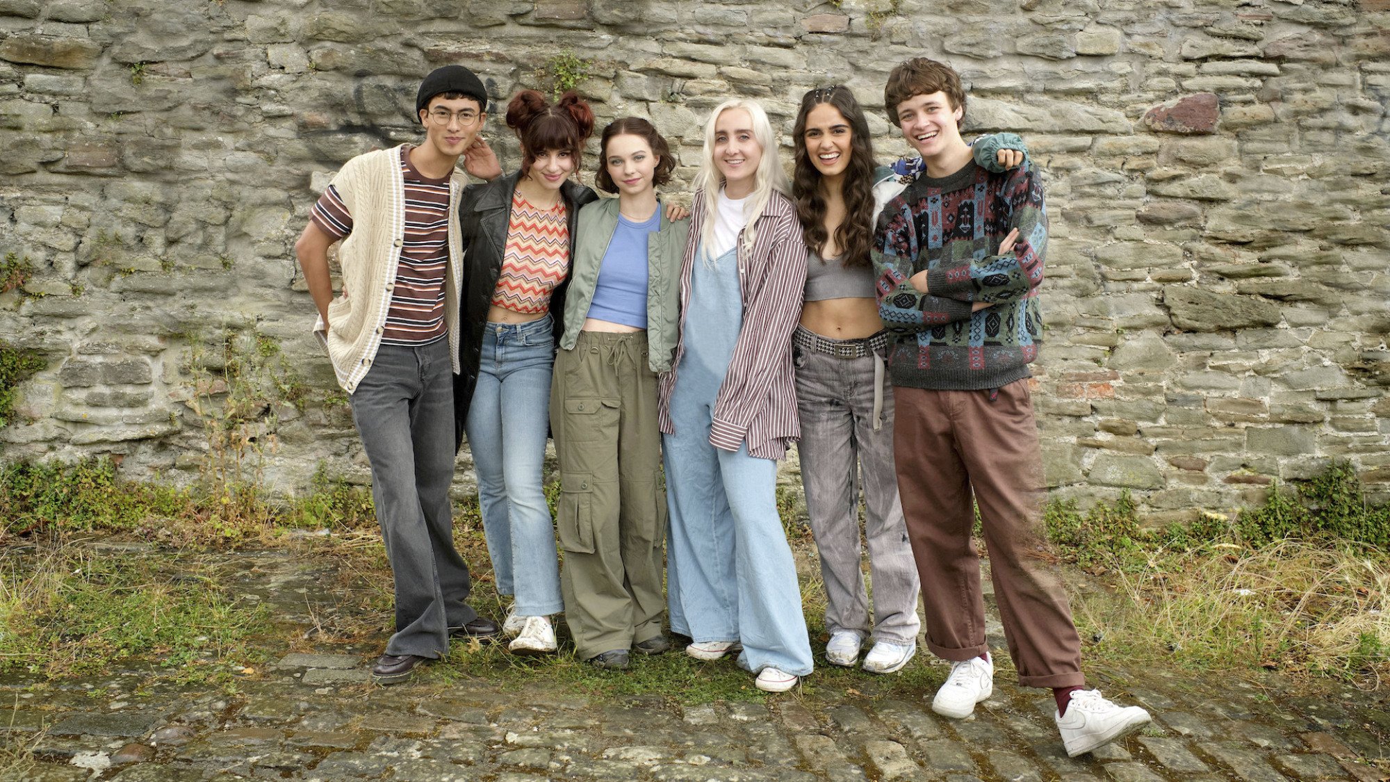 A group of teens stand in front of an old brick wall.