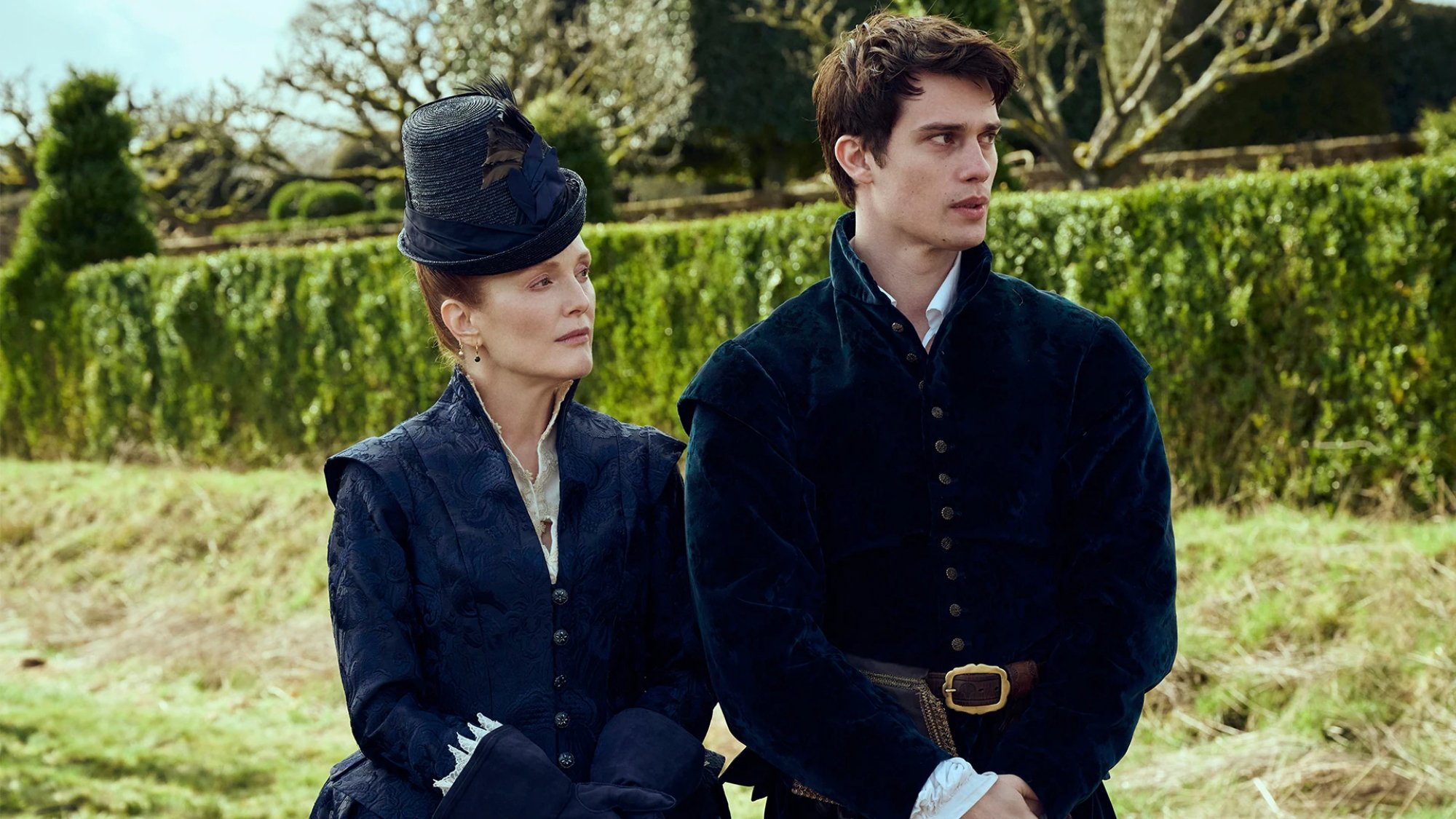 A man and woman in regal dress stand in a garden.