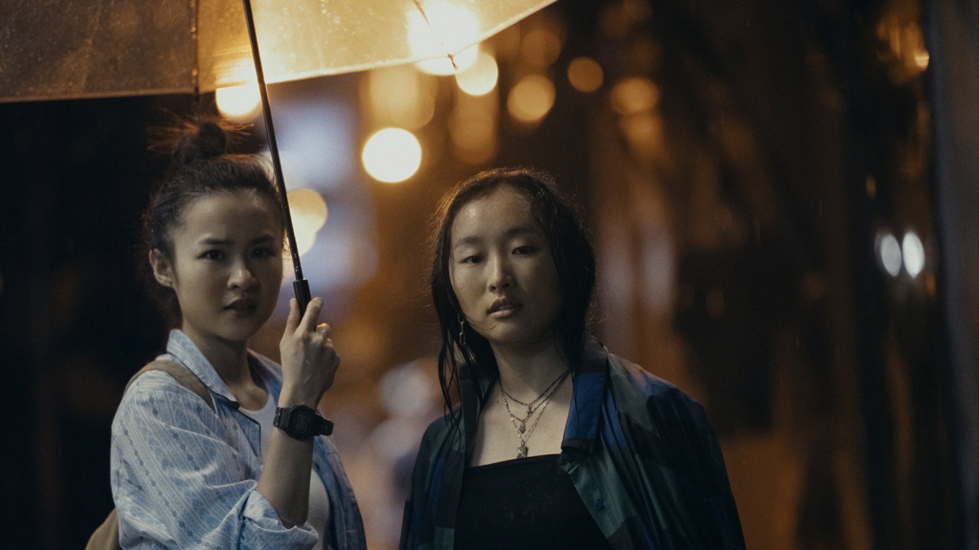Two women standing under a clear umbrella in the middle of a rainy street.