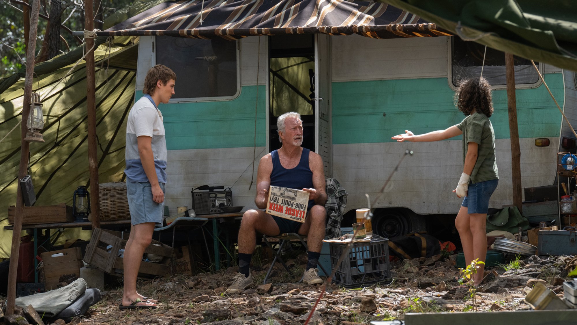 Two boys stand confronting an older man at his caravan.