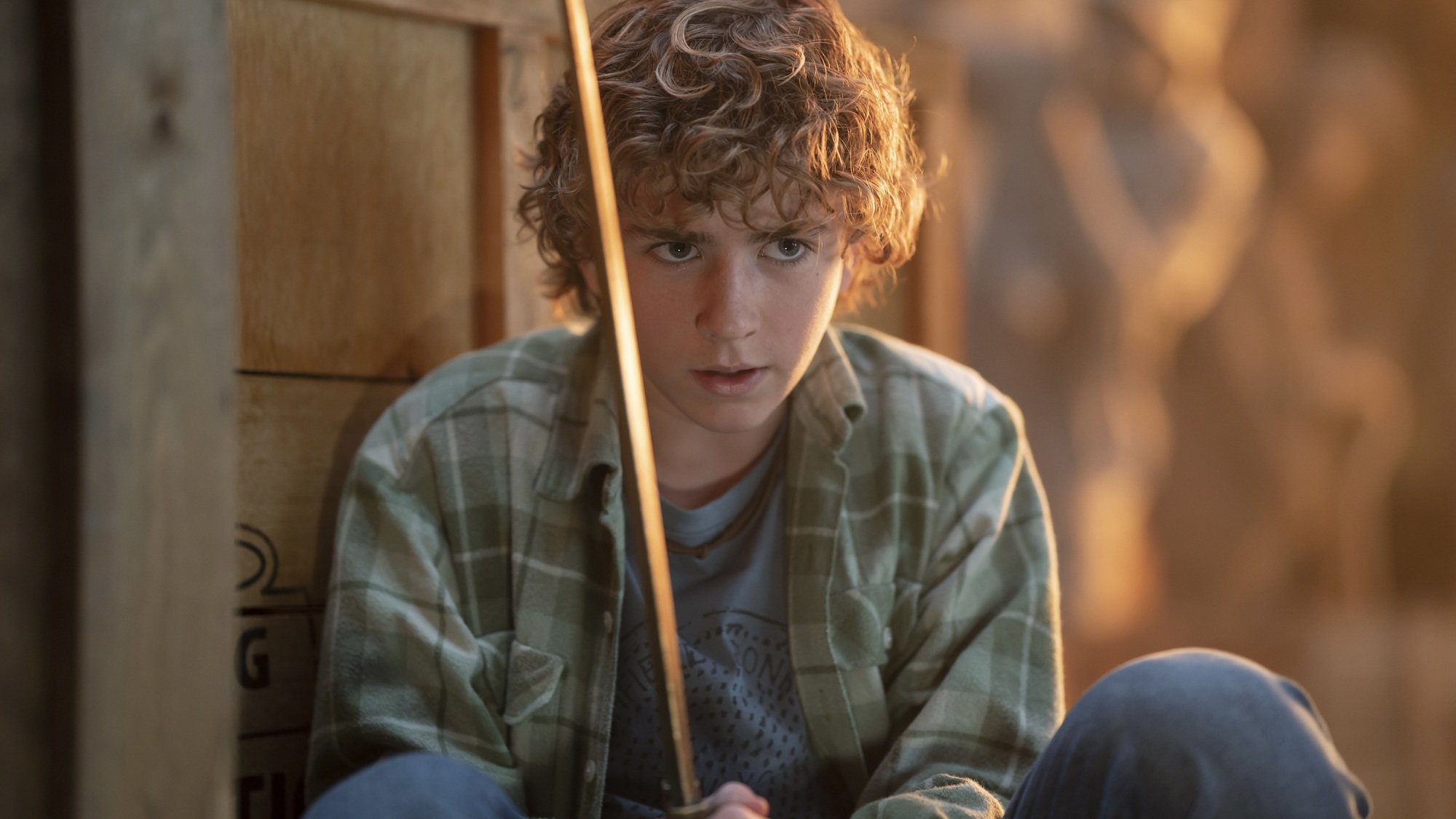 A young boy grips a gold sword while hiding behind a crate.