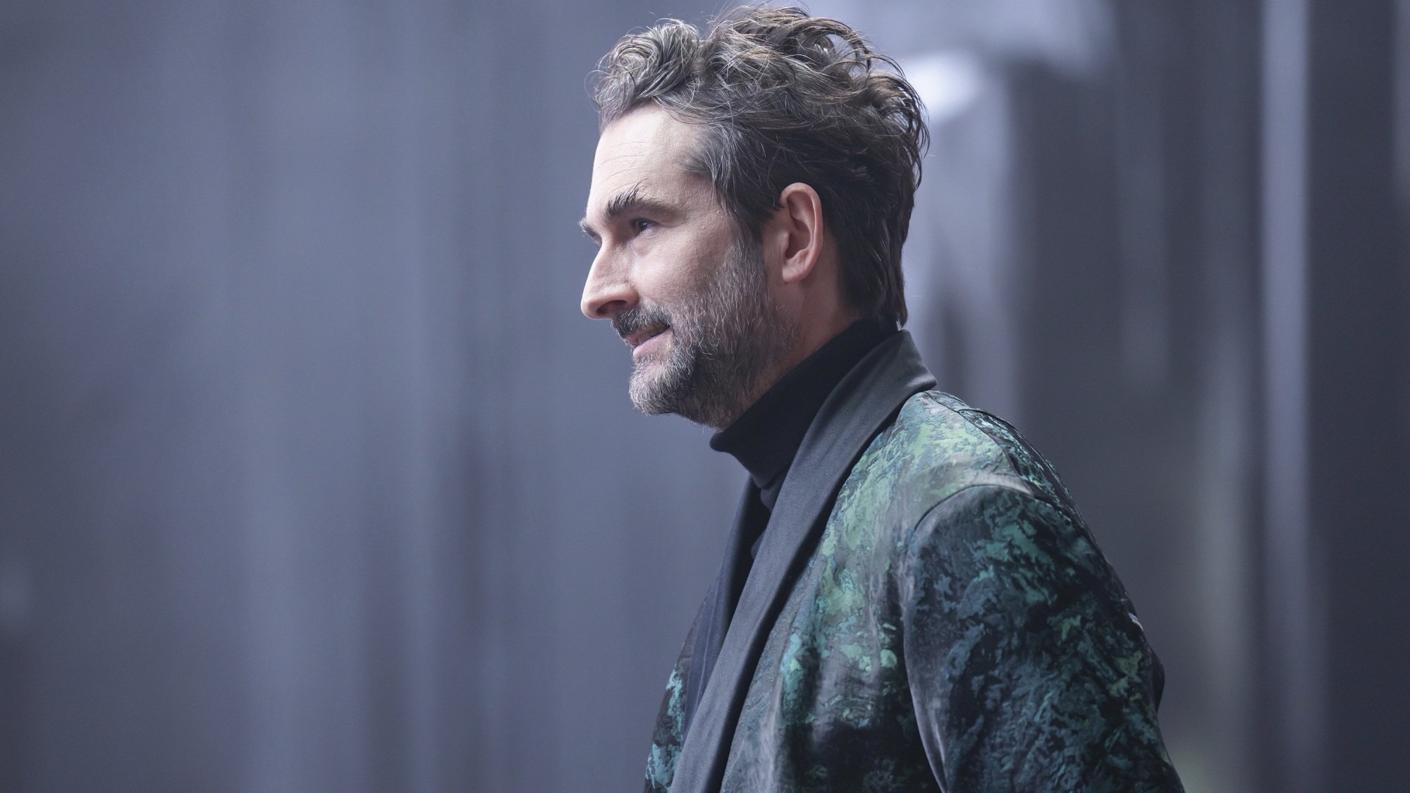 A man in a green and black robe in a dark palace.