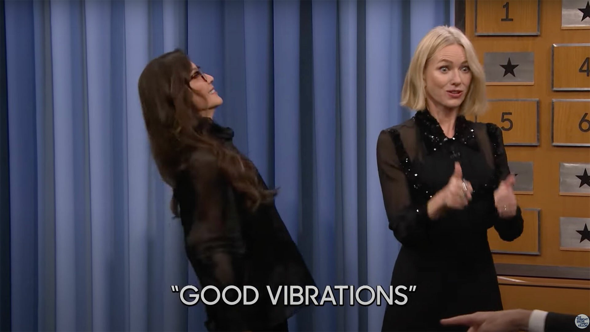 Two women stand up playing charades.