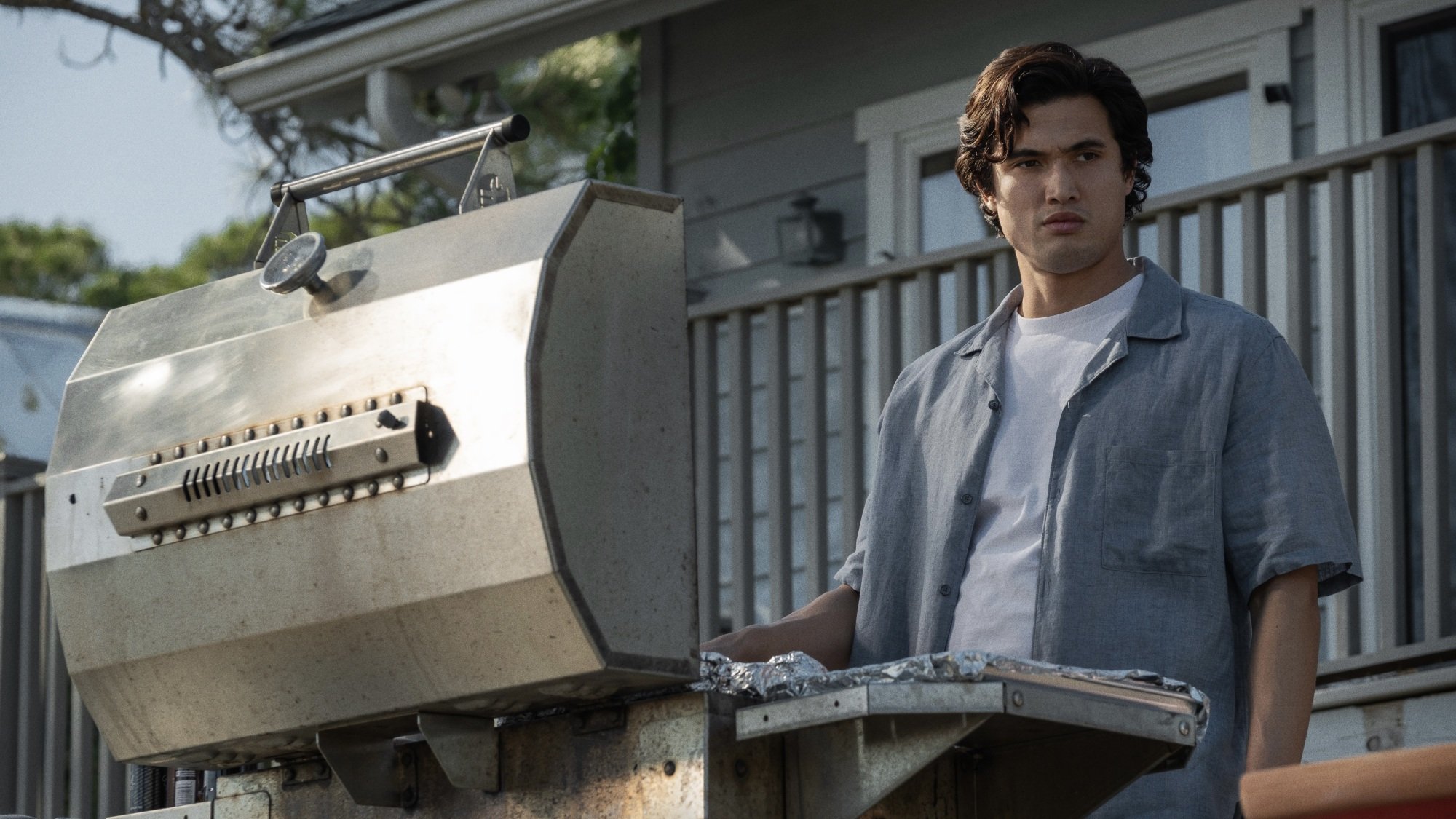 A man in a grey button down grilling hot dogs.