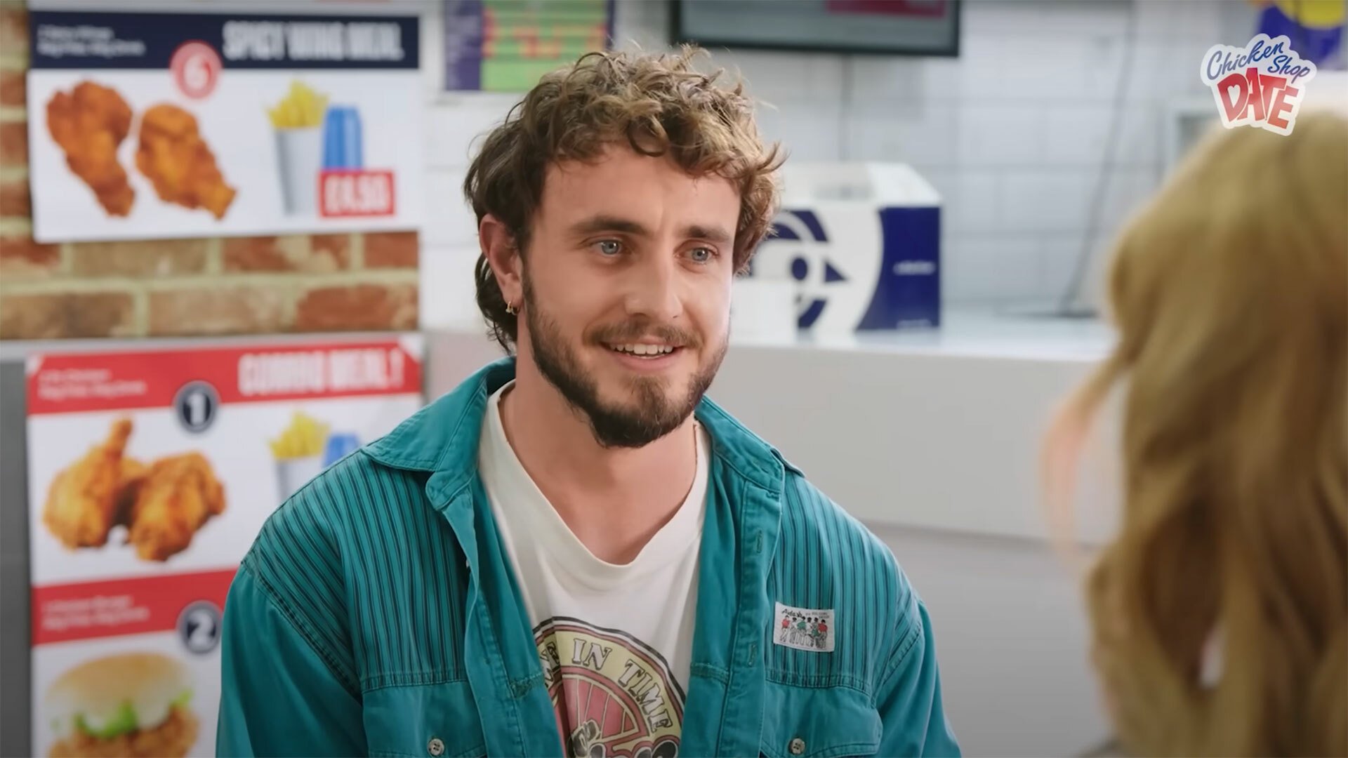 A bearded man sits at a table in a chicken shop.