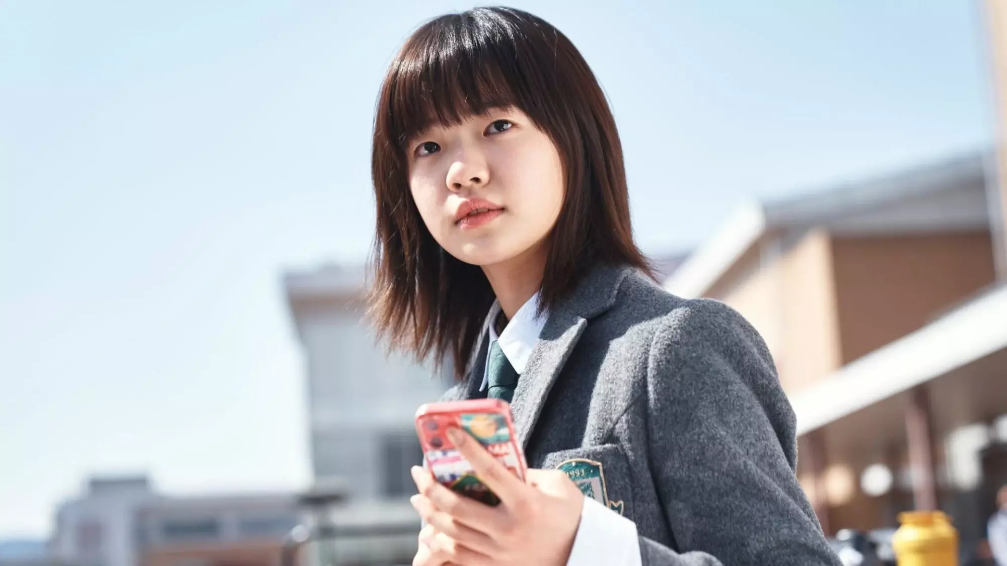 A teen girl in a school uniform holds her cell phone.