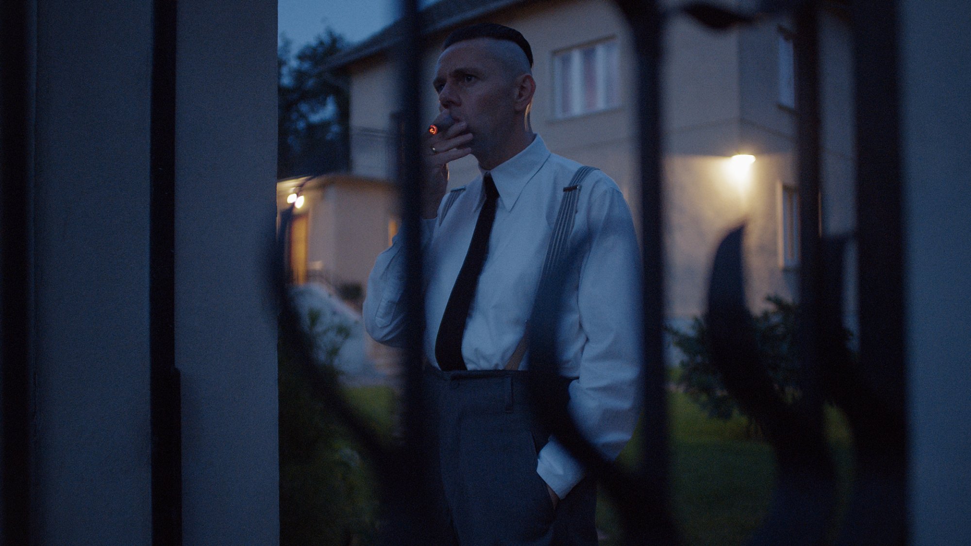 A man in a white shirt and tie smokes a cigarette at night time.