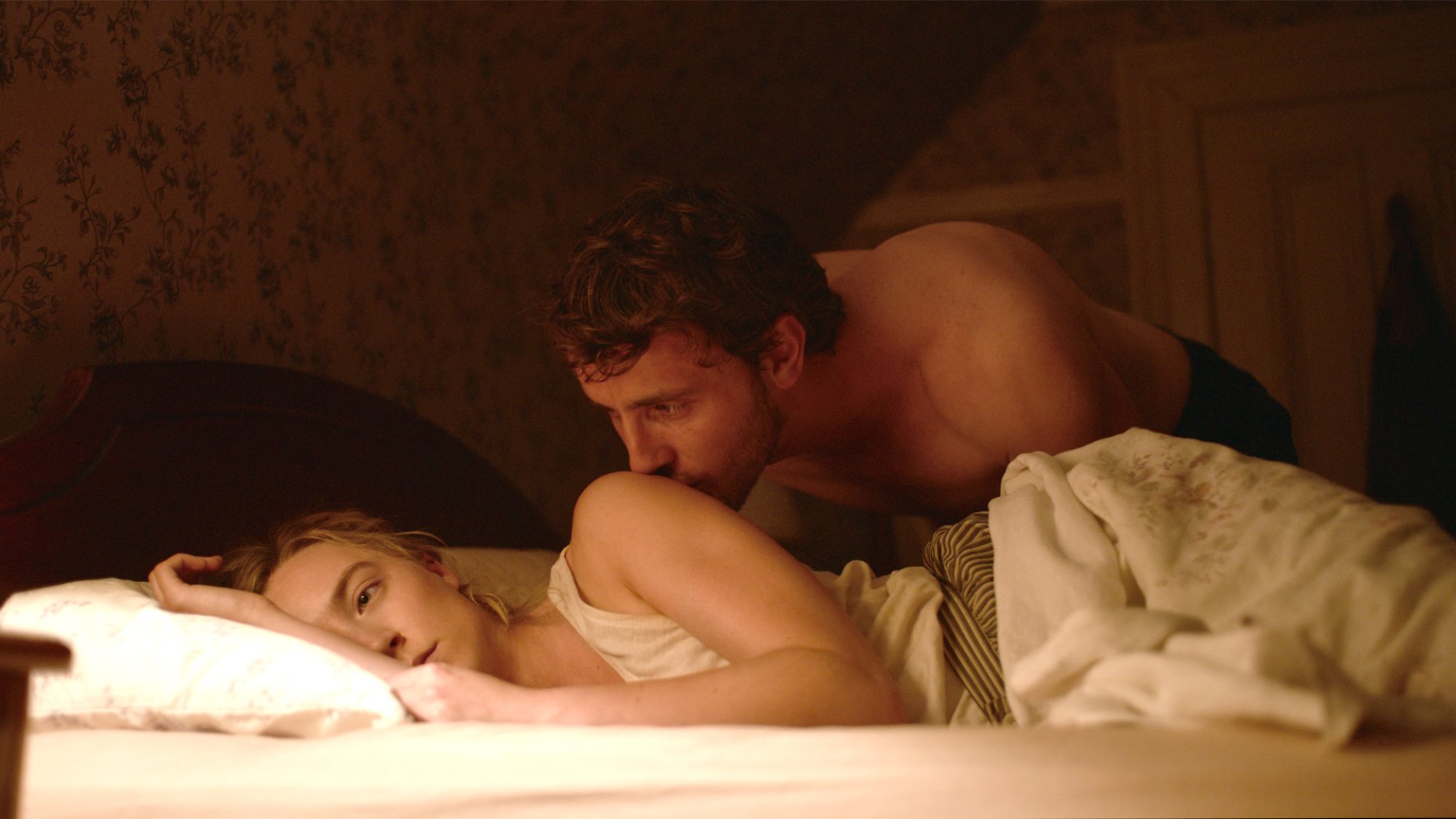 A woman lies in bed ignoring a man kissing her shoulder.