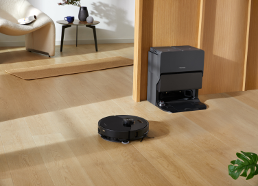 Black Roborock S8 robot vacuum cleaning hardwood floor with dock and furniture in background