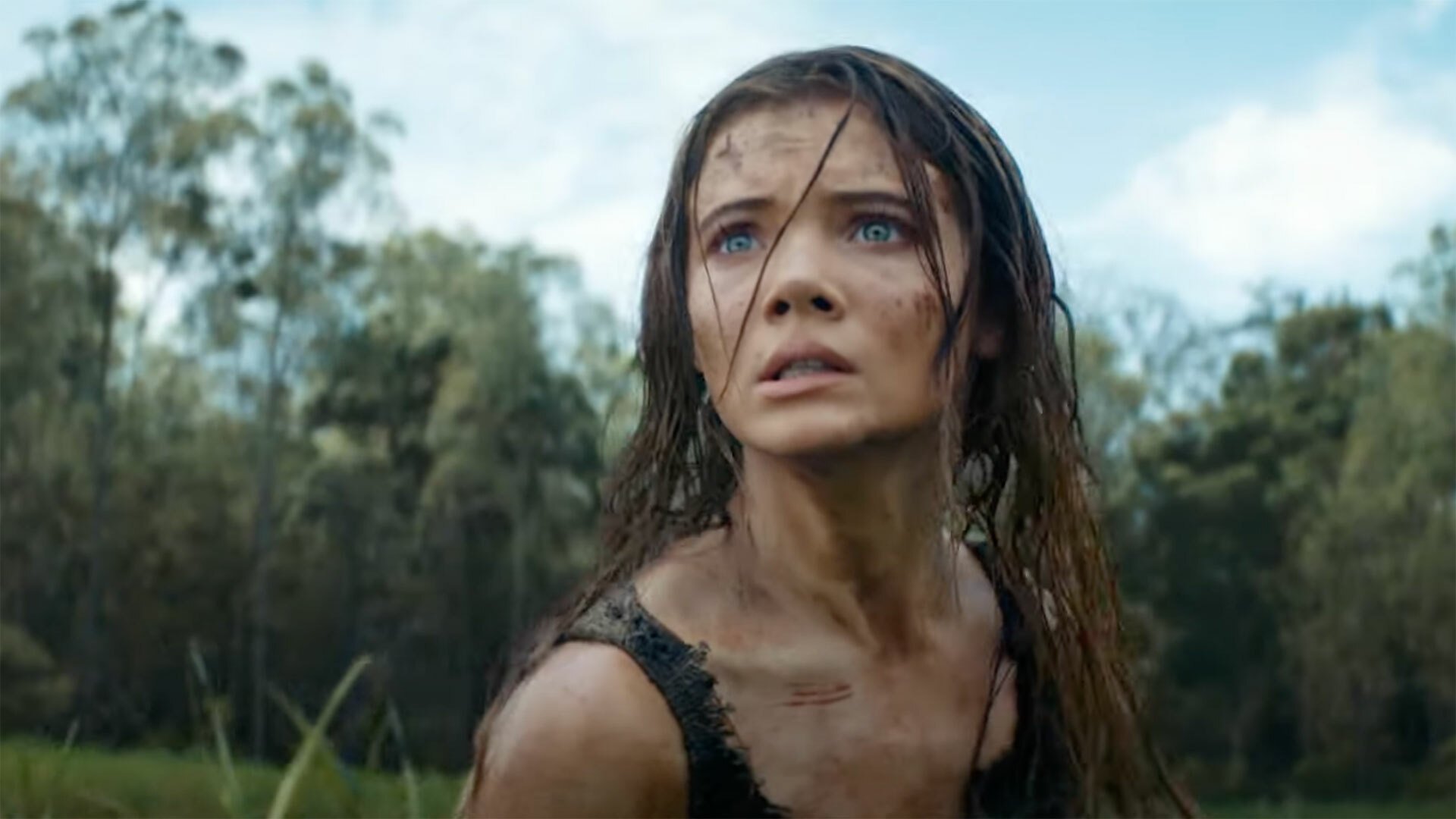 A dishevelled woman stands in a field, looking scared.