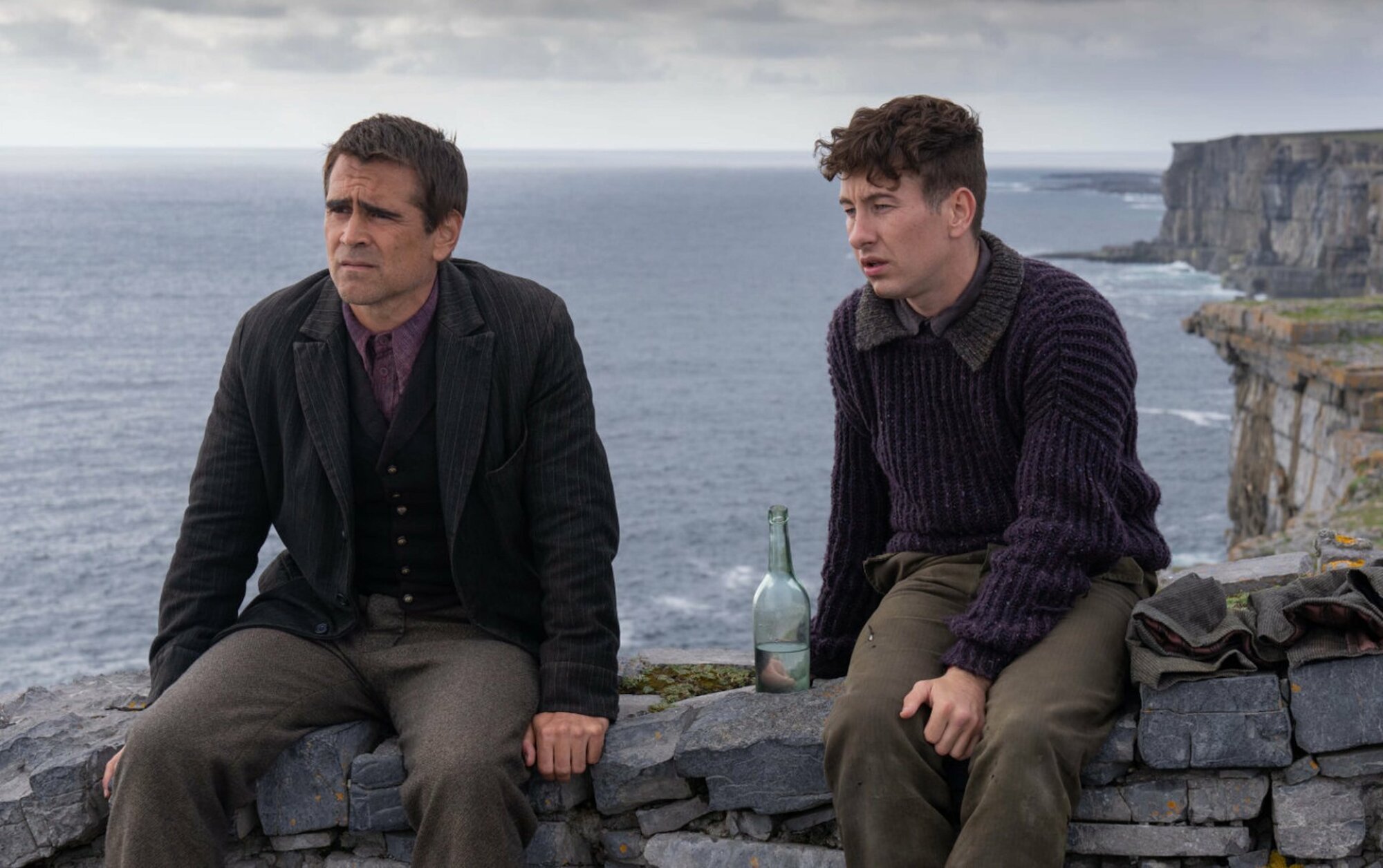 Colin Farrell and Barry Keoghan sit on a stone wall with their backs facing the water in "The Banshees of Inisherin."