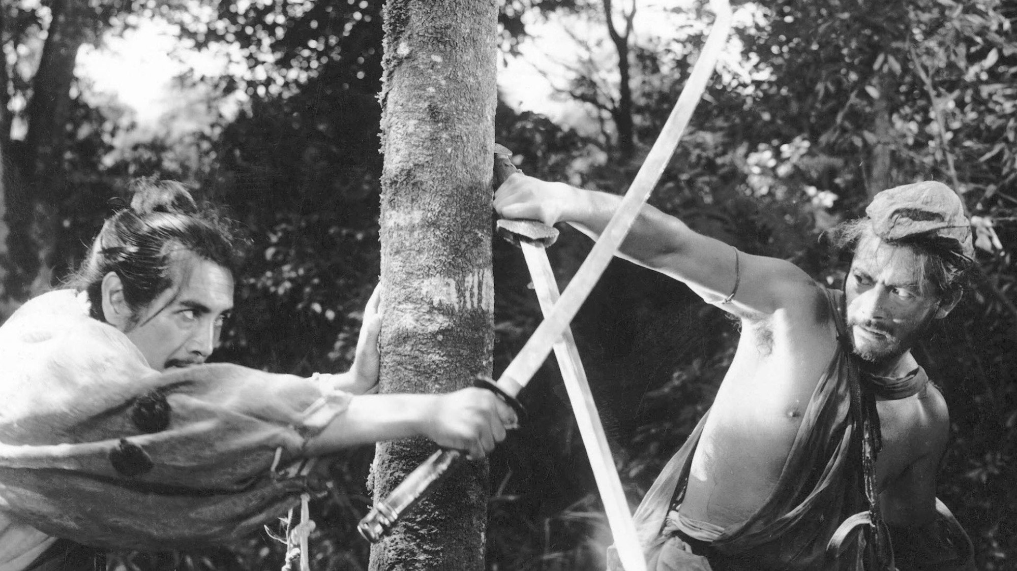 Two men fight with swords in a forest.