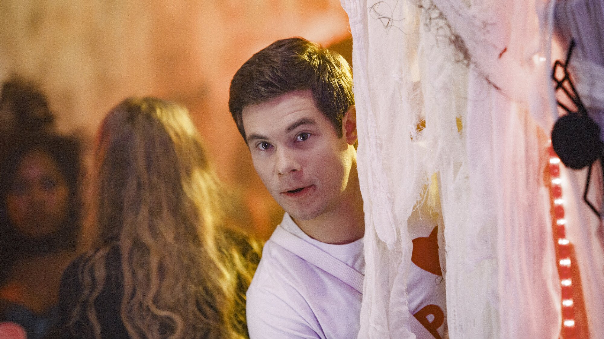 A man peeks behind a white curtain at a party. 