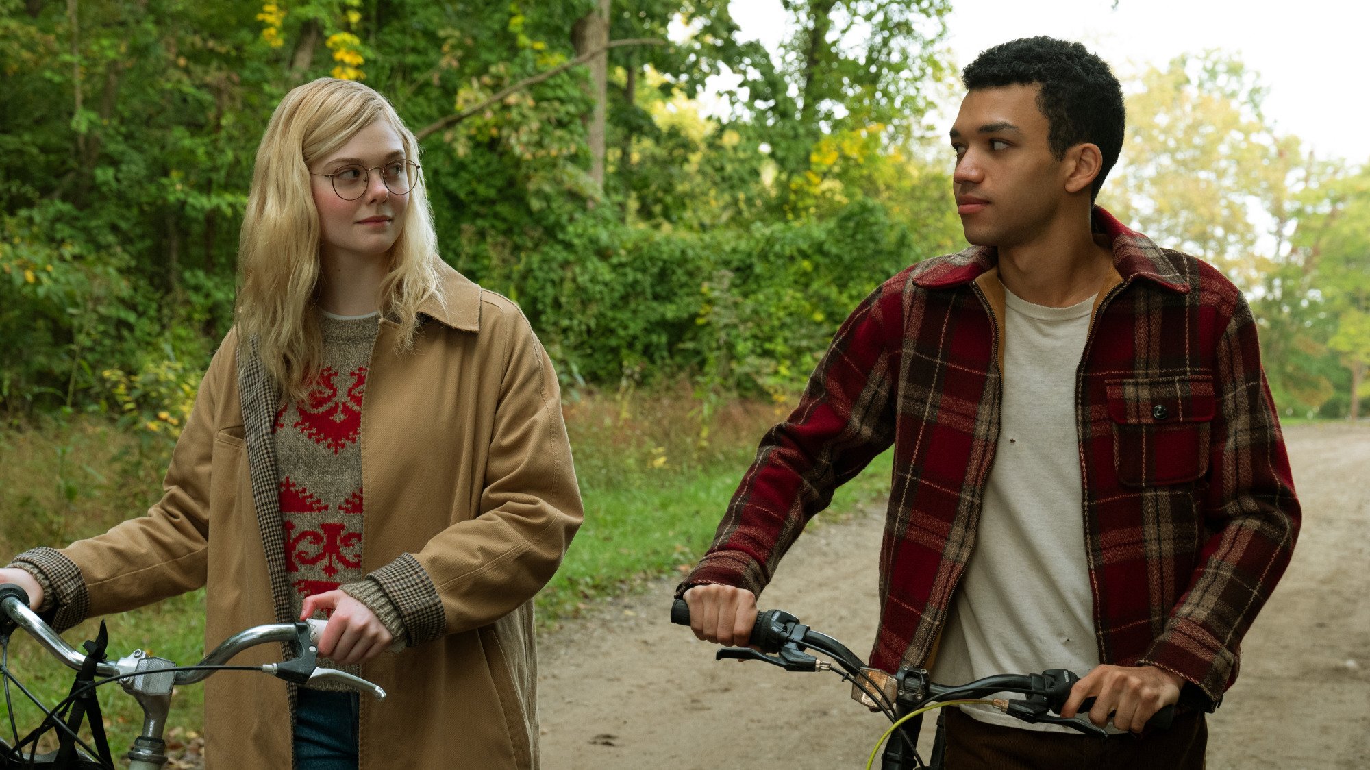 Two teenagers ride bikes in a forest. 