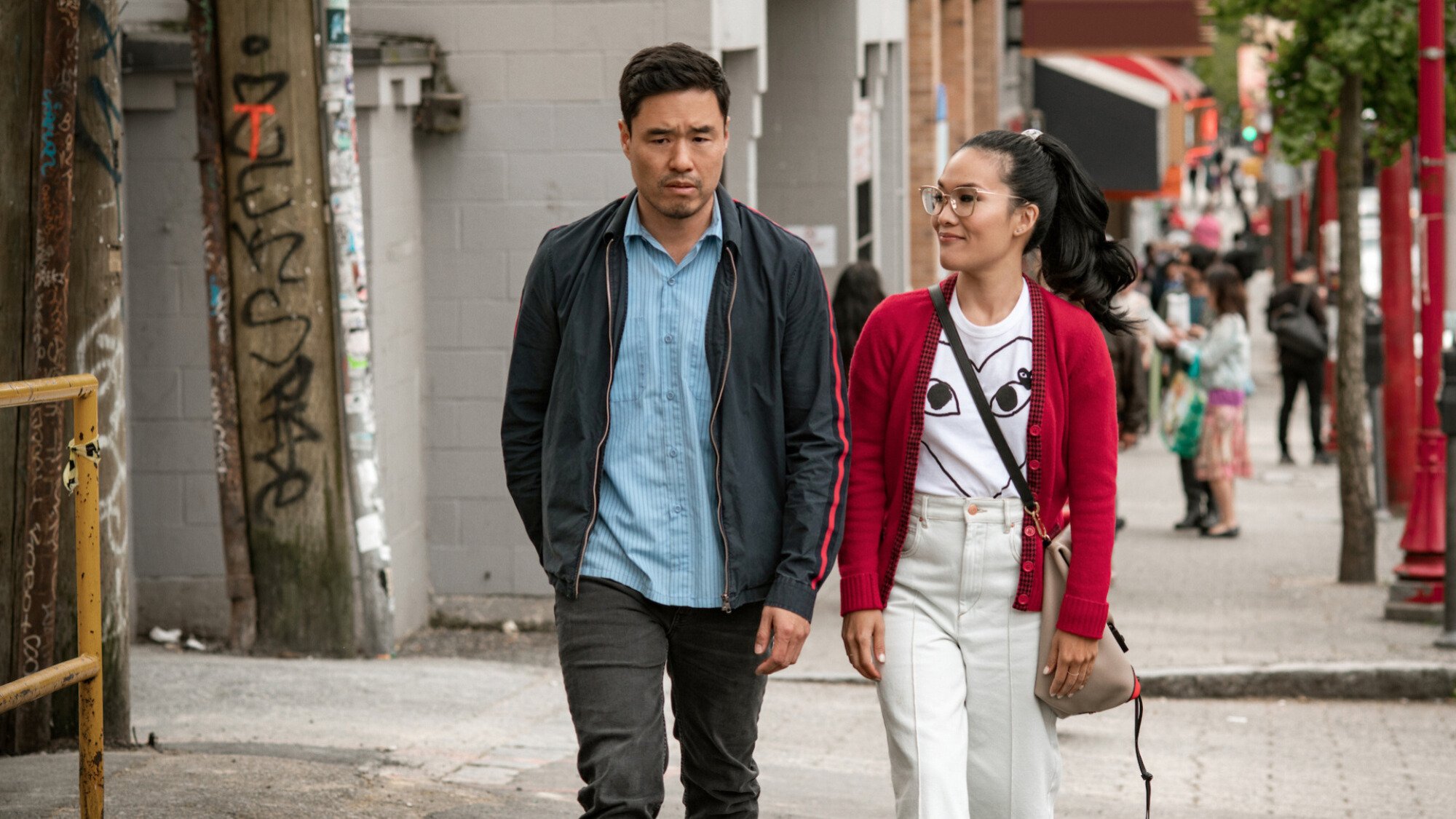 A man and a woman walk on a street while talking.