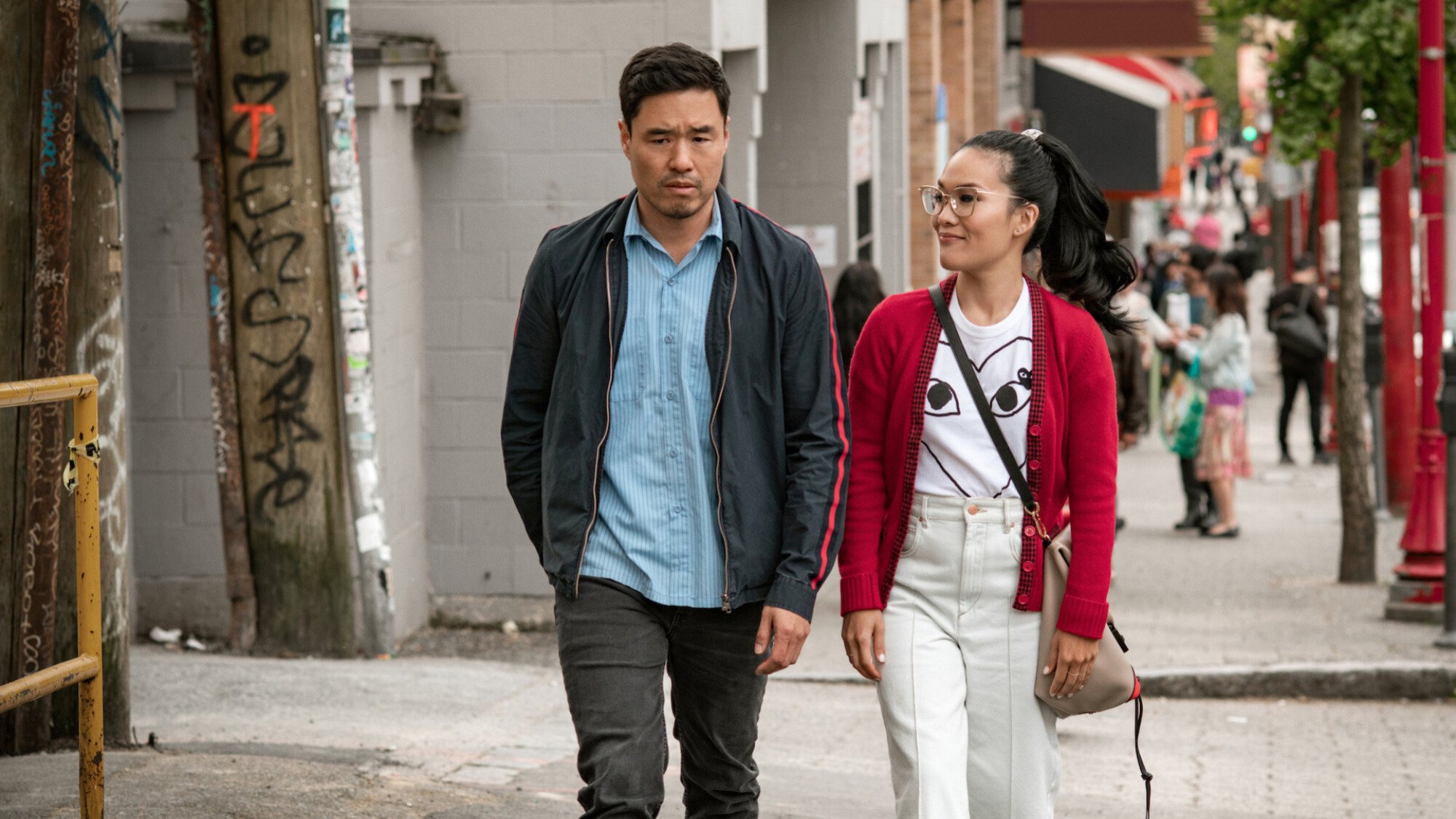 A man and a woman walk on a street while talking. 