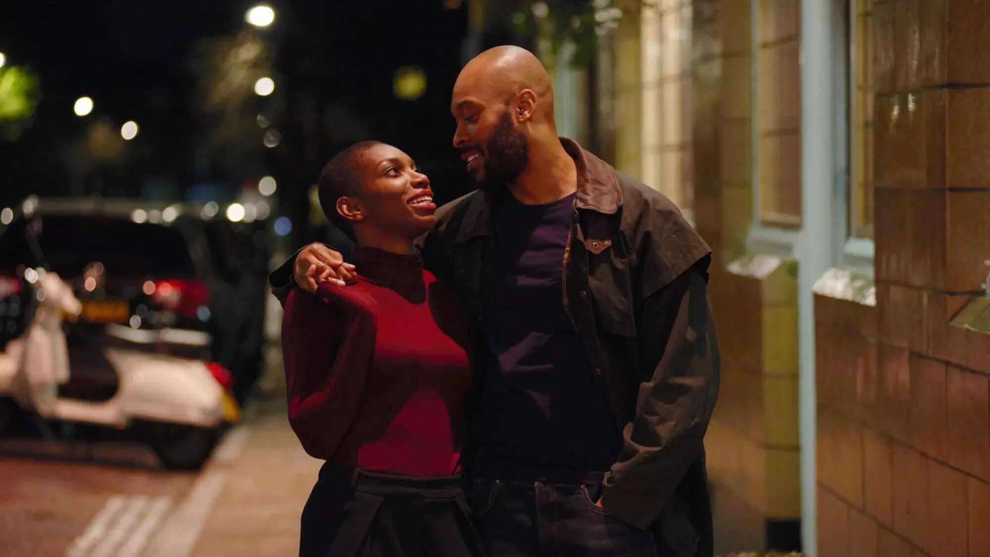 A young couple embraces while walking on the street at night. 