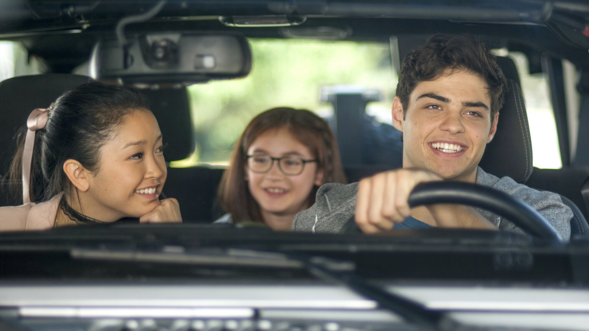 Two teenagers and a child laugh in a car. 