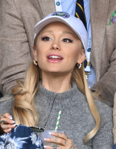 Ariana Grande with blonde eyebrows and hair, in a white cap and grey sweater.