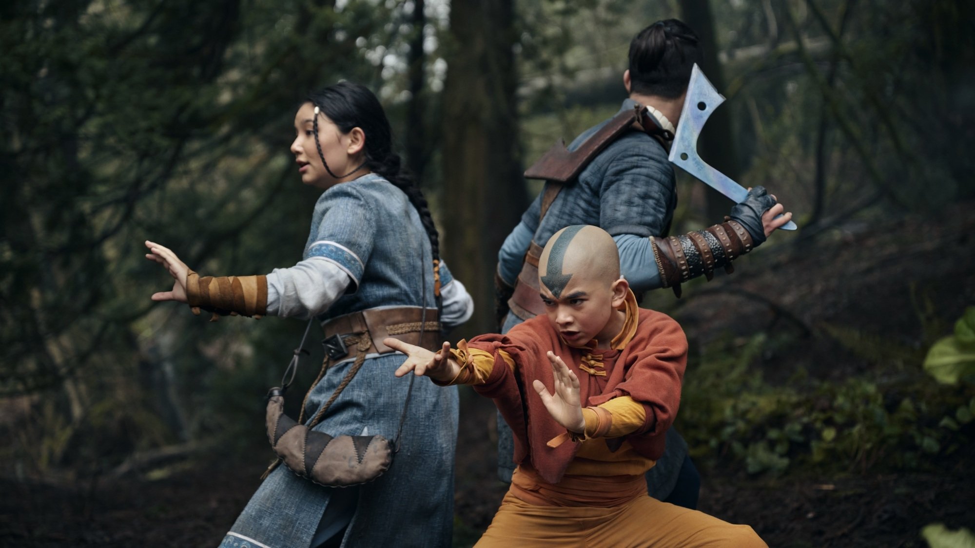 Katara, Aang, and Sokka stand back to back in fighting stances.