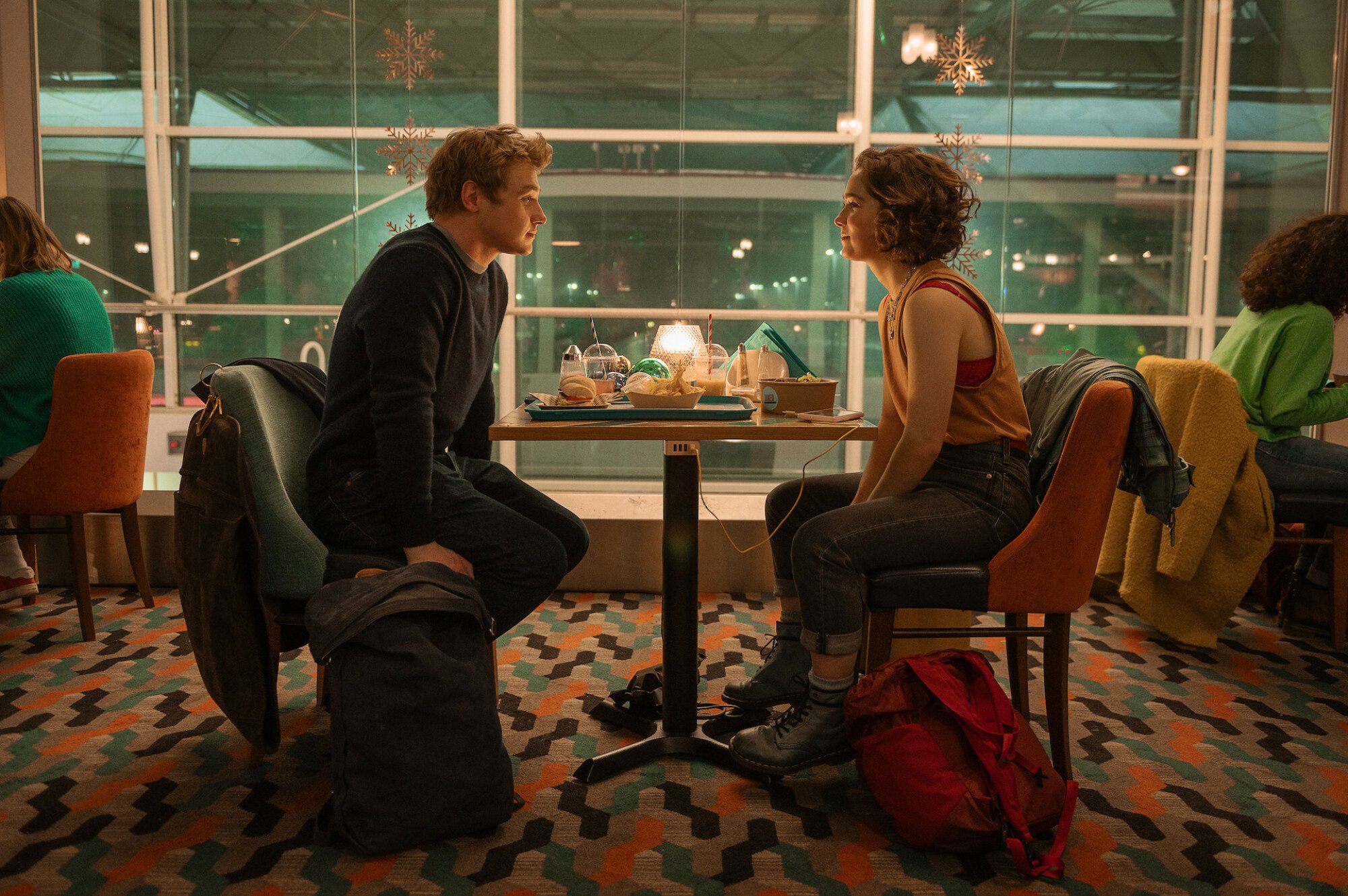 A boy and a girl sit facing each other at a table in an airport restaurant.