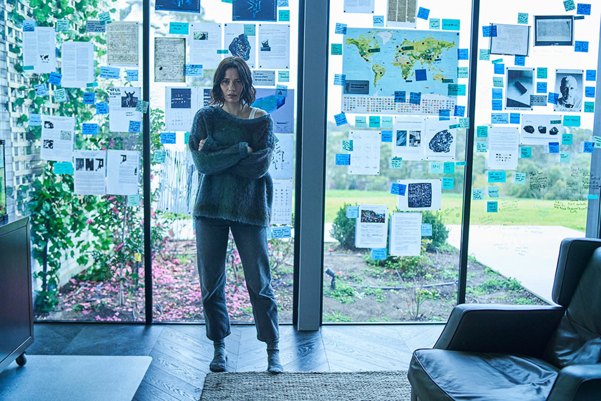 A woman stands in front of a large window with paper taped all over it.