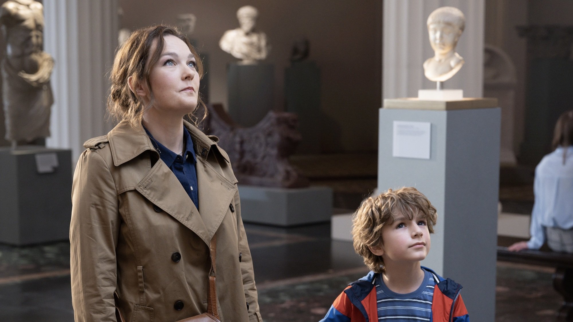 A woman and her young son in a hall of statues in a museum.