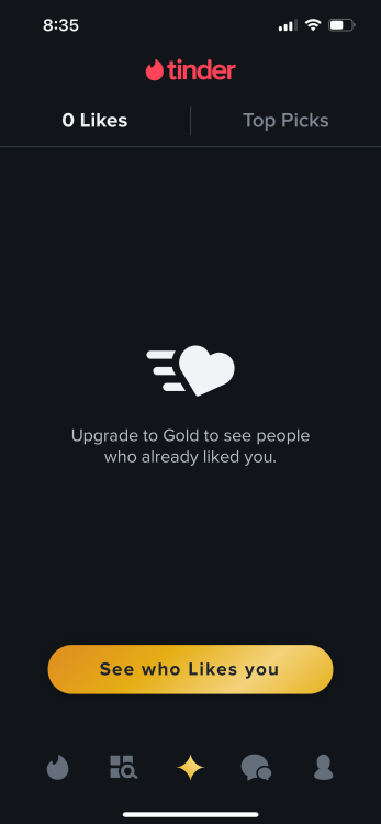 The image displays a screen from the Tinder app indicating that the user has zero likes. The top of the screen shows the time as 8:35, the Tinder logo, and mobile network and battery indicators. The screen features a large heart with motion lines and text underneath that reads "Upgrade to Gold to see people who already liked you." There is a large yellow button at the bottom saying "See who Likes you" with navigation icons for different app features at the very bottom of the screen. The tabs "0 Likes" and "Top Picks" are at the top of the screen.