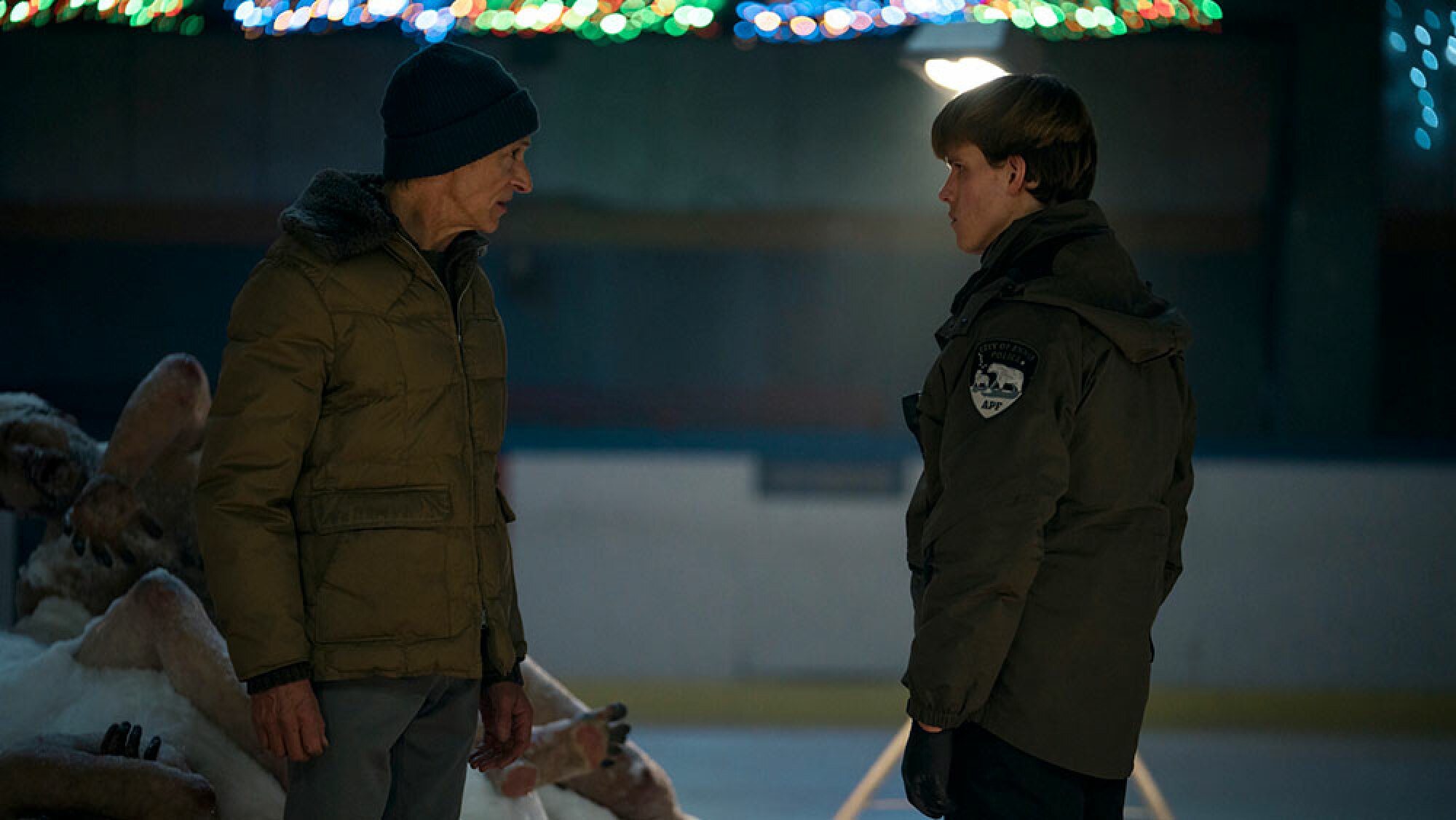 Two police officers stand in the middle of an ice rink, facing each other.
