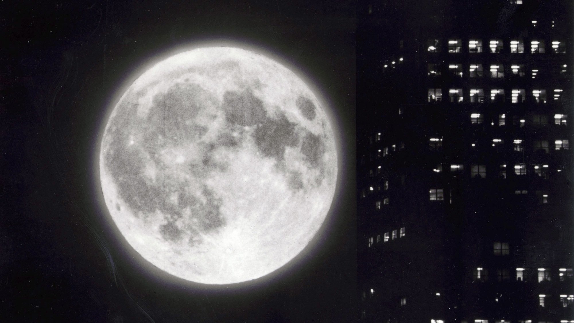 A full moon shines next to a skyscraper.