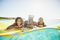 a family with three people lays on a floating mat on the ocean