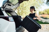 a woman puts a black suitcase into the trunk of a white car