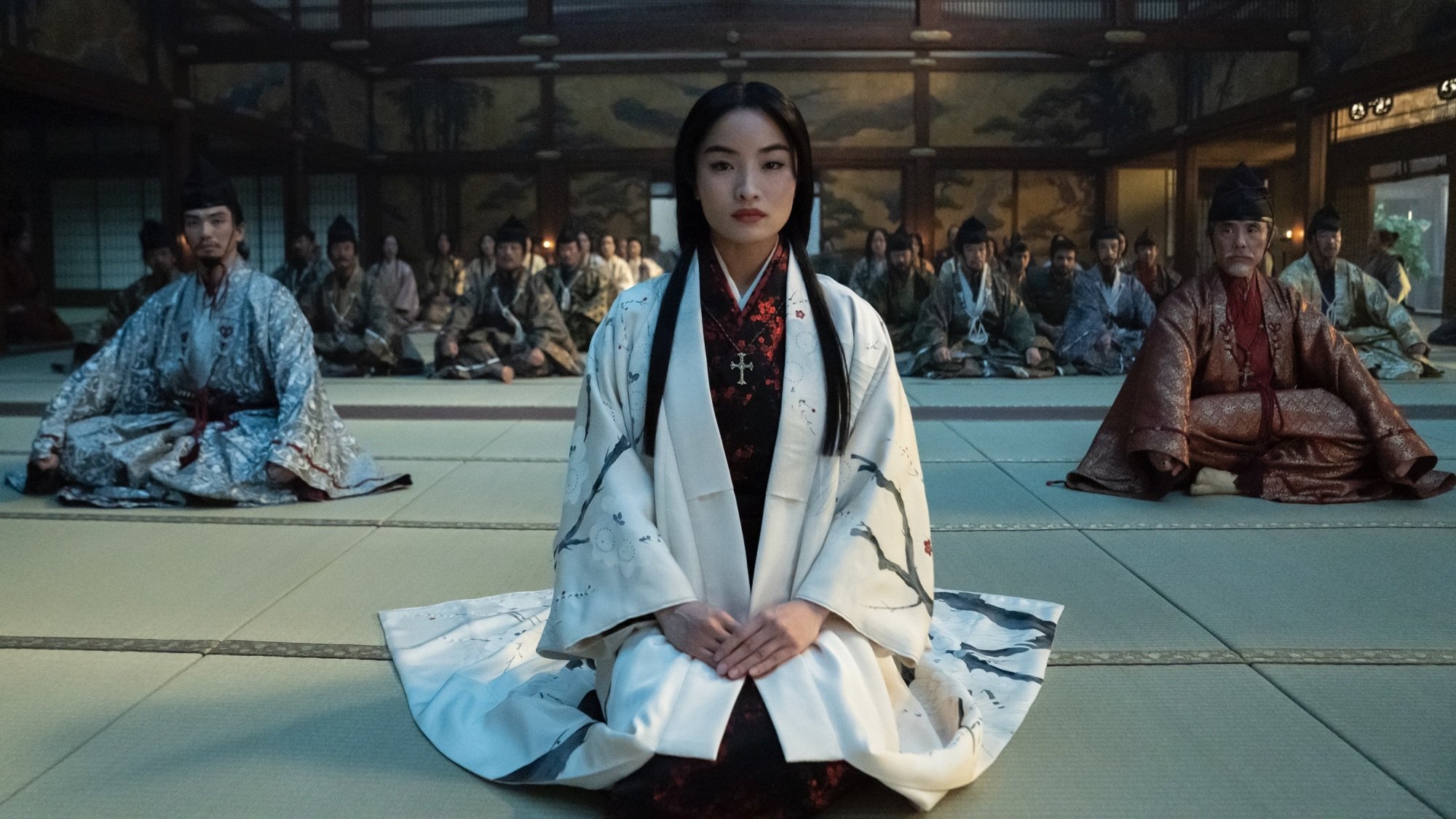 Toda Mariko sits in the middle of a crowded castle hall, dressed in white.
