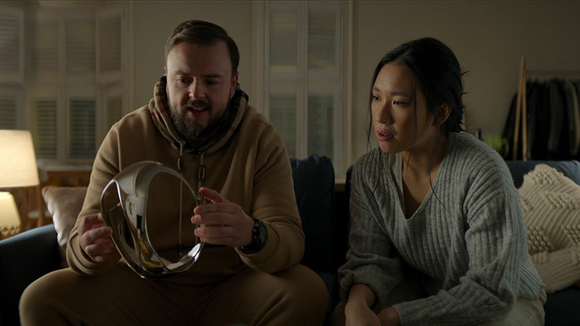 A man and a woman sit on a sofa staring at a shiny headset.