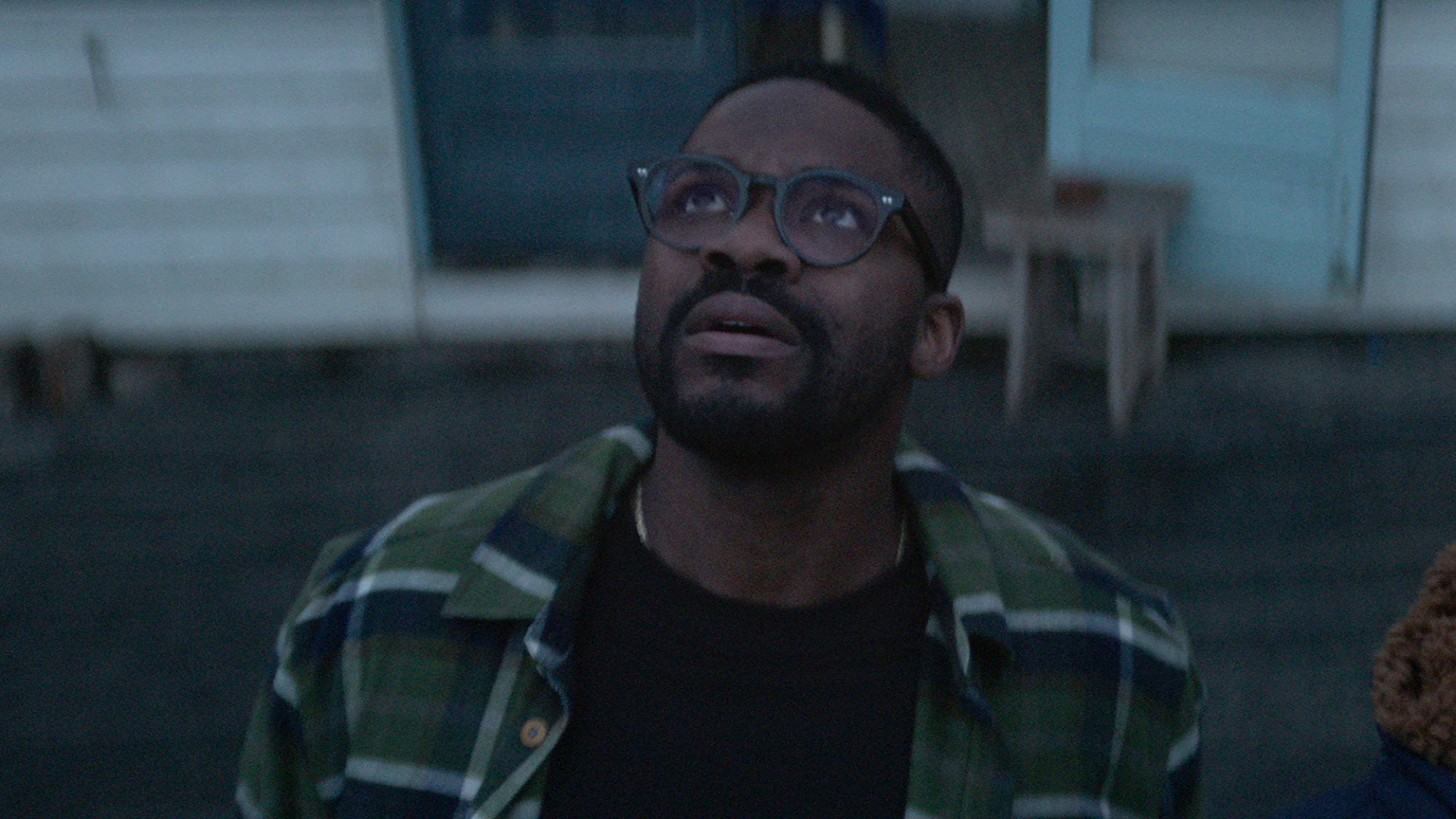 A man with glasses stares at the sky with a worried look.