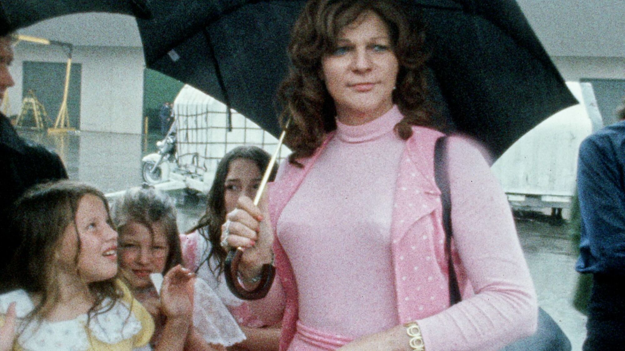 A woman in pink stands with her children under an umbrella.