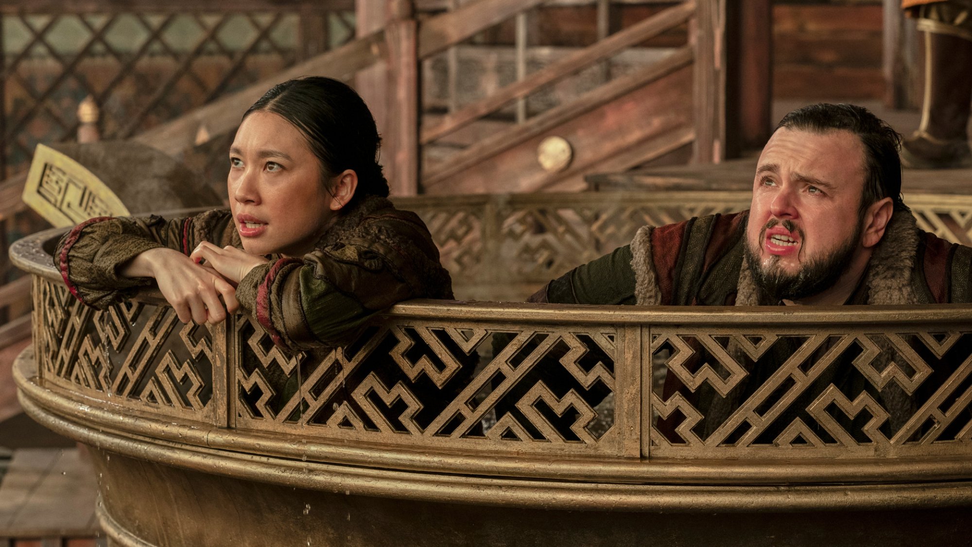 Two people in outfits from China's Yuan dynasty sit ina. giant cauldron looking worried.