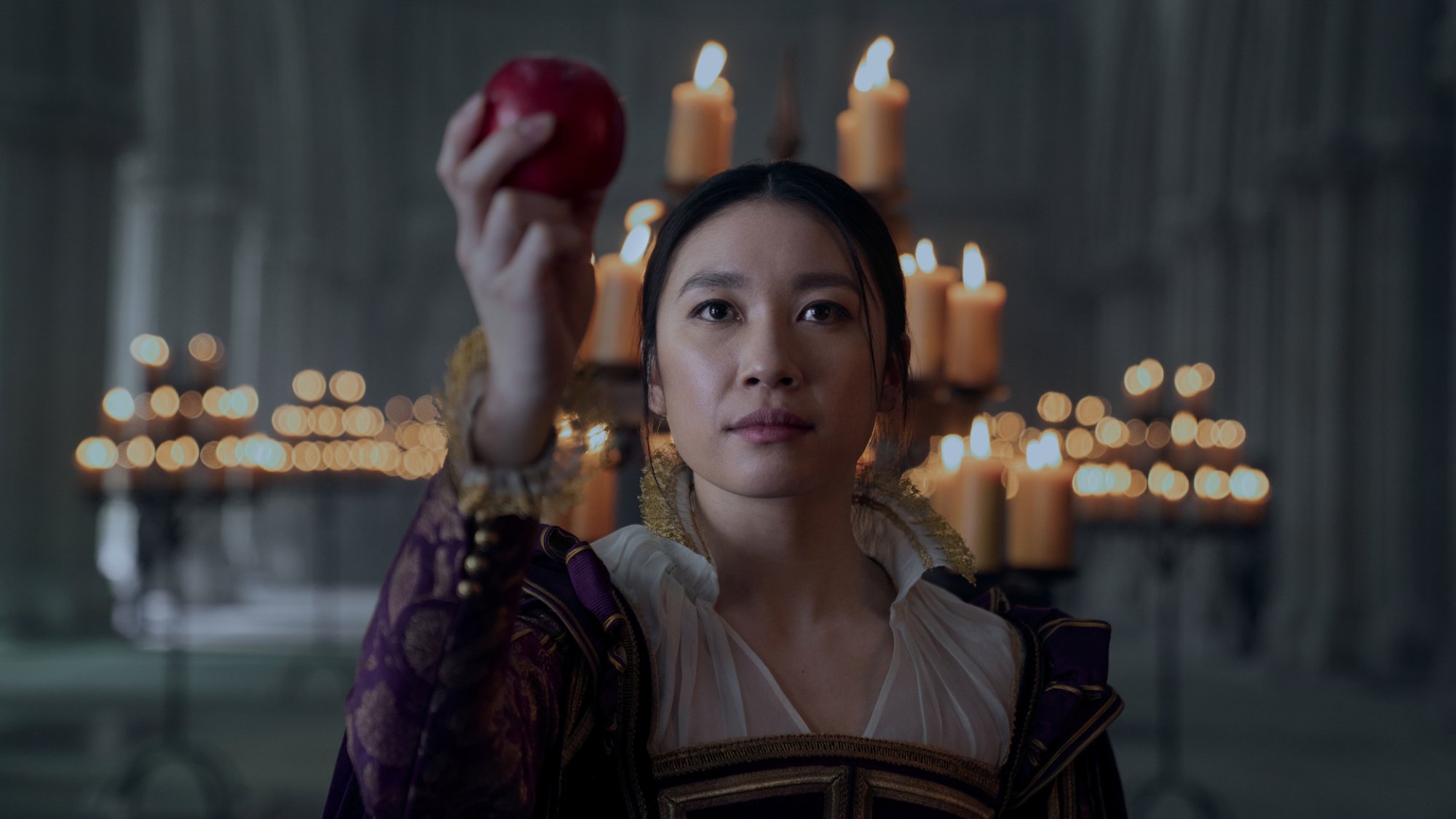 A woman holds up an apple in front of a candelabra.