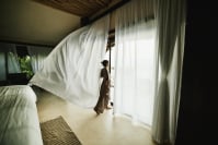 a woman looks out of a hotel door with drapes blowing into the wind
