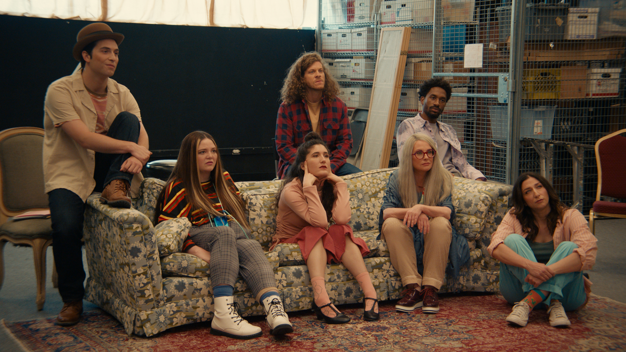 A group of actors sit on a couch in a rehearsal room.