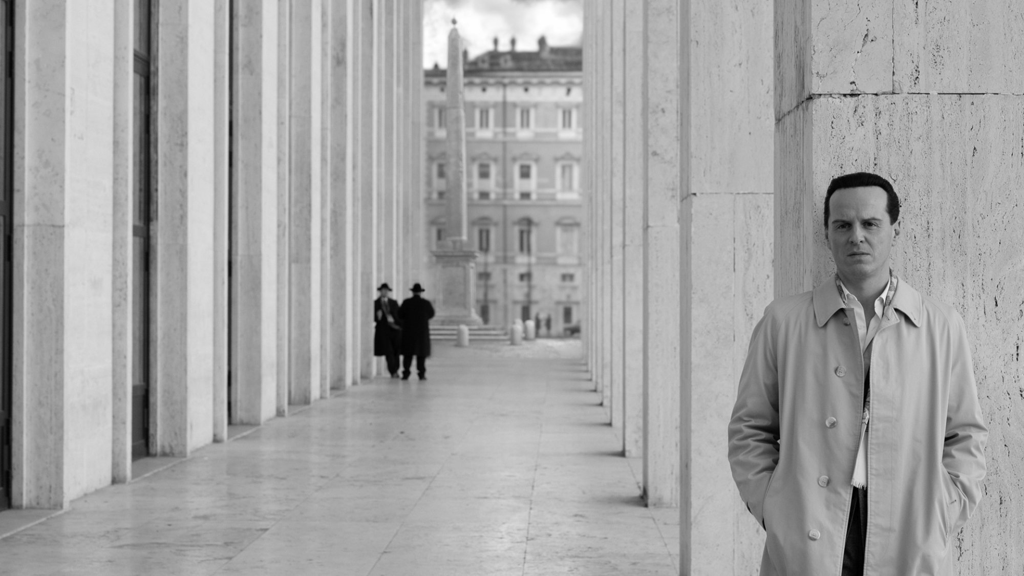 A man stands in a long open corridor.